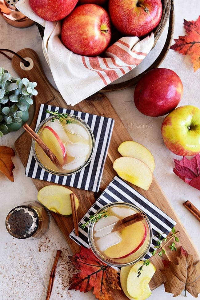 apple cider cocktails with fall leaves and fresh apples around the glasses