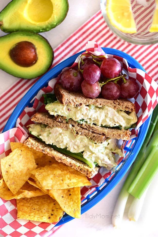 avocado chicken salad sandwich cut in half in a basket with grapes and chips