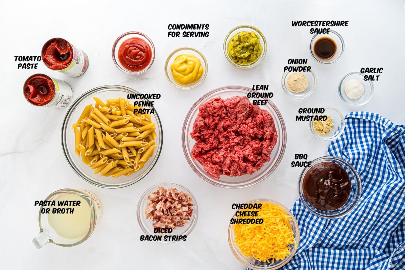 Ingredients for Bacon Cheeseburger Pasta Skillet arranged on a countertop, including penne pasta, ground beef, bacon, tomato paste, and cheddar cheese.