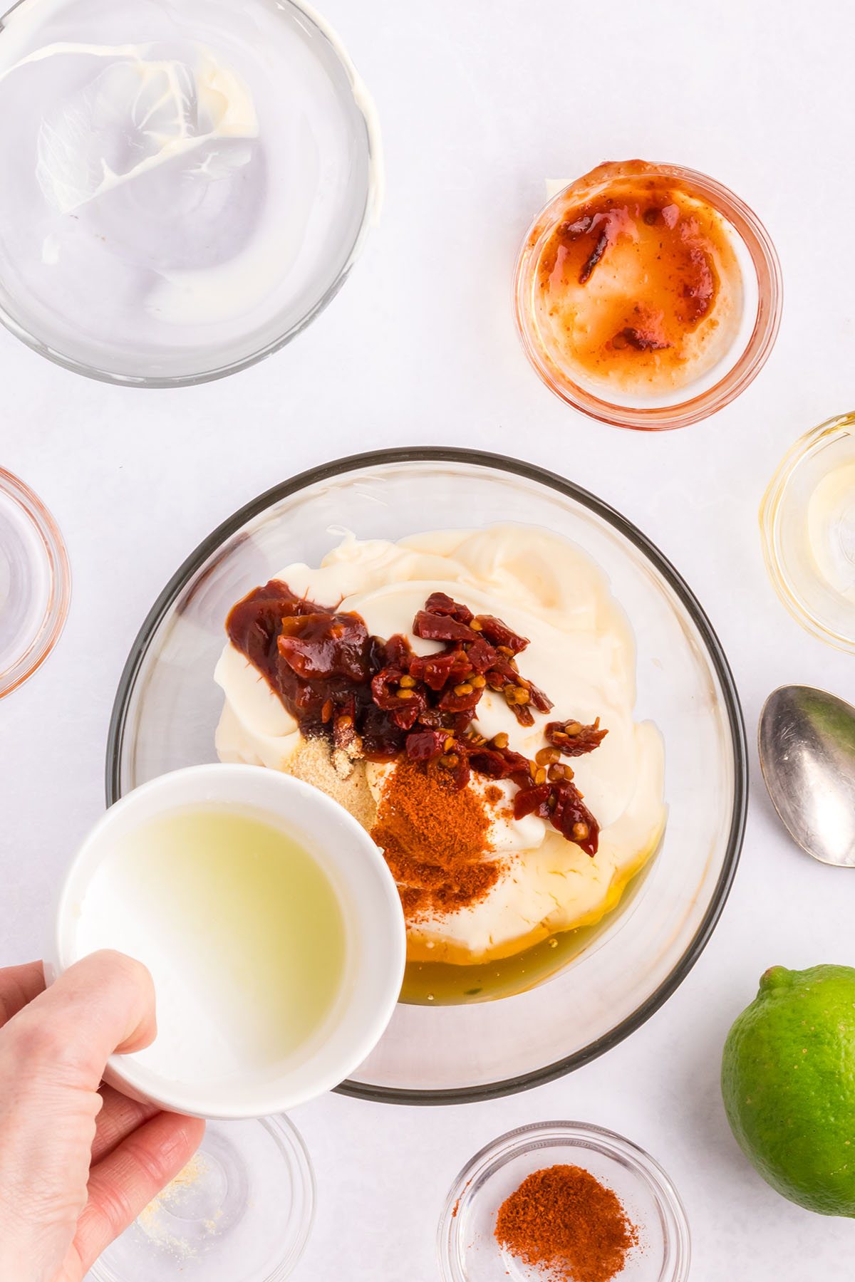 adding chipotle mayo ingredients to a glass mixing bowl.