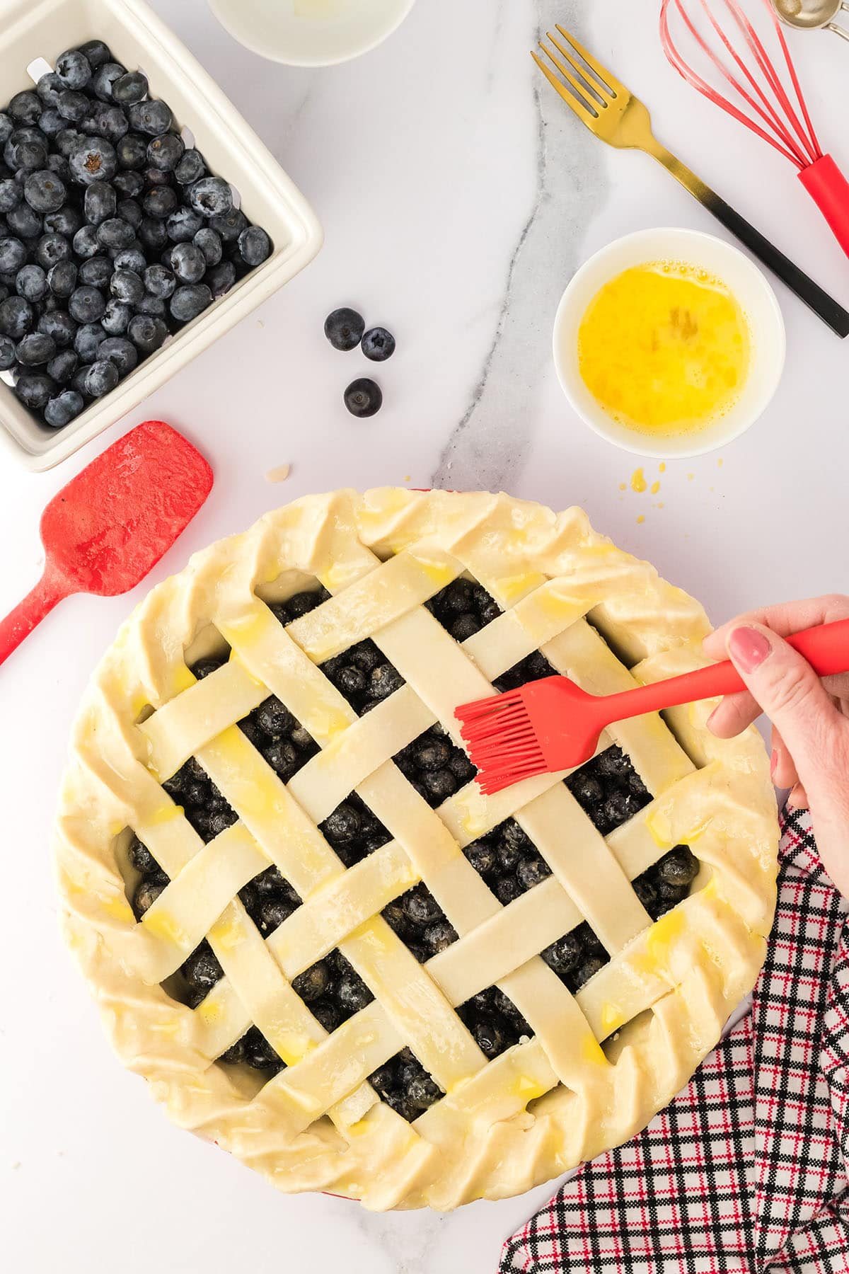 brushing egg wash on a pie crust with a red pastry brush