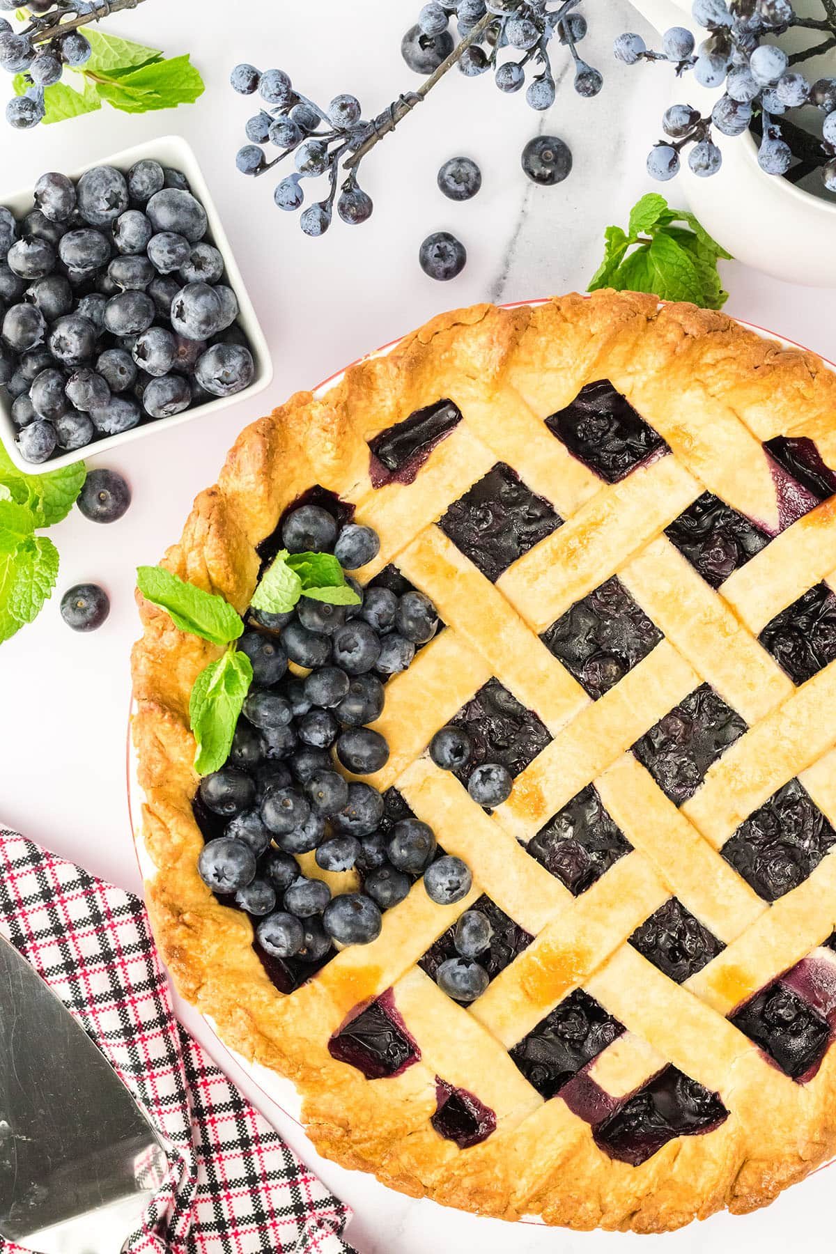 a blueberry pie with fresh blueberries and mint on top of the lattice crust