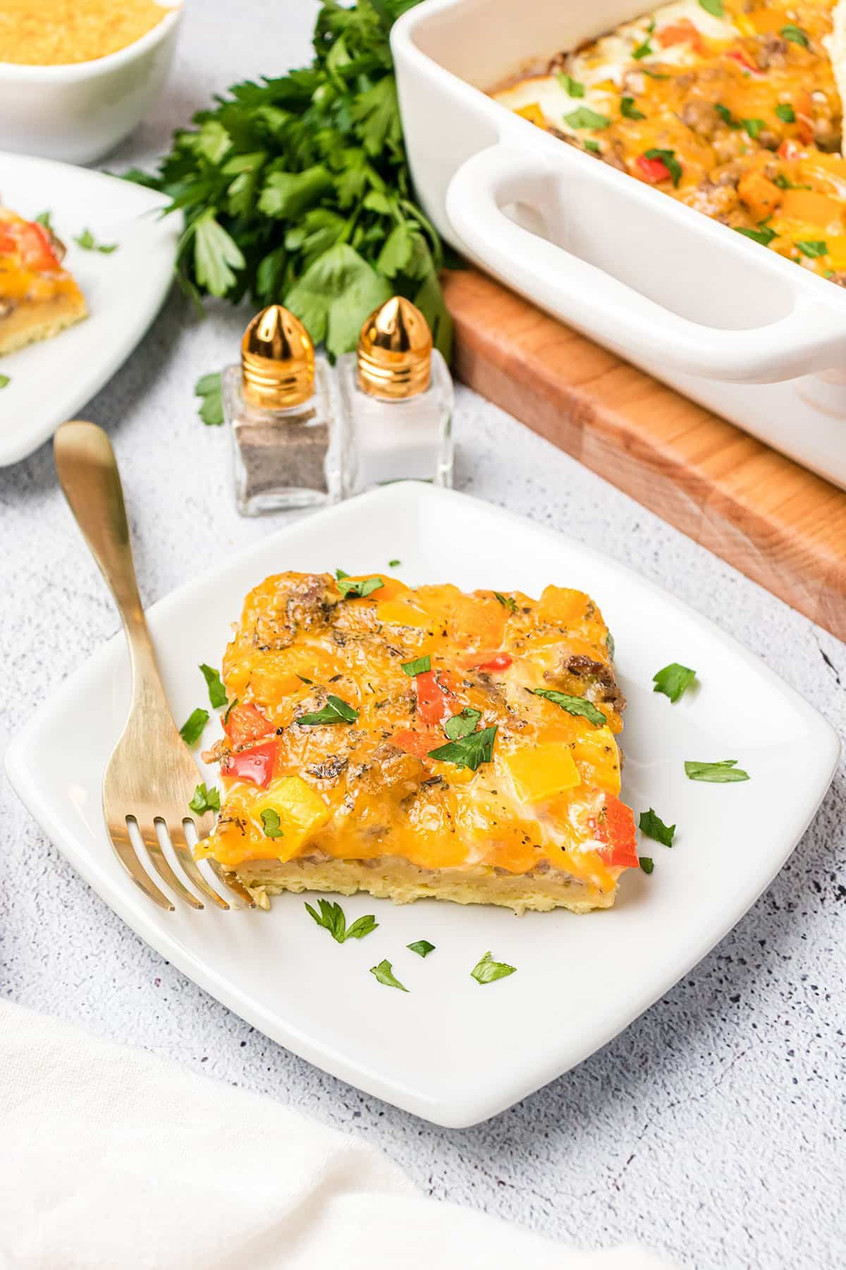 egg casserole serving on a plate next to the casserole dish