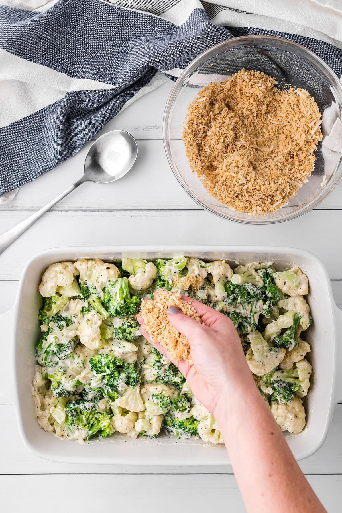 woman's hand sprinkling breadcrumb topping over casserole