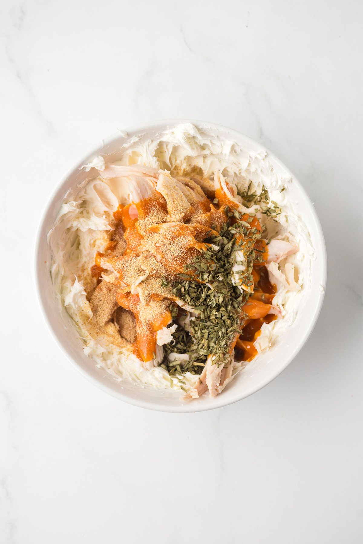Shredded chicken, cream cheese, buffalo sauce, garlic powder, and dried chives in a bowl before mixing.
