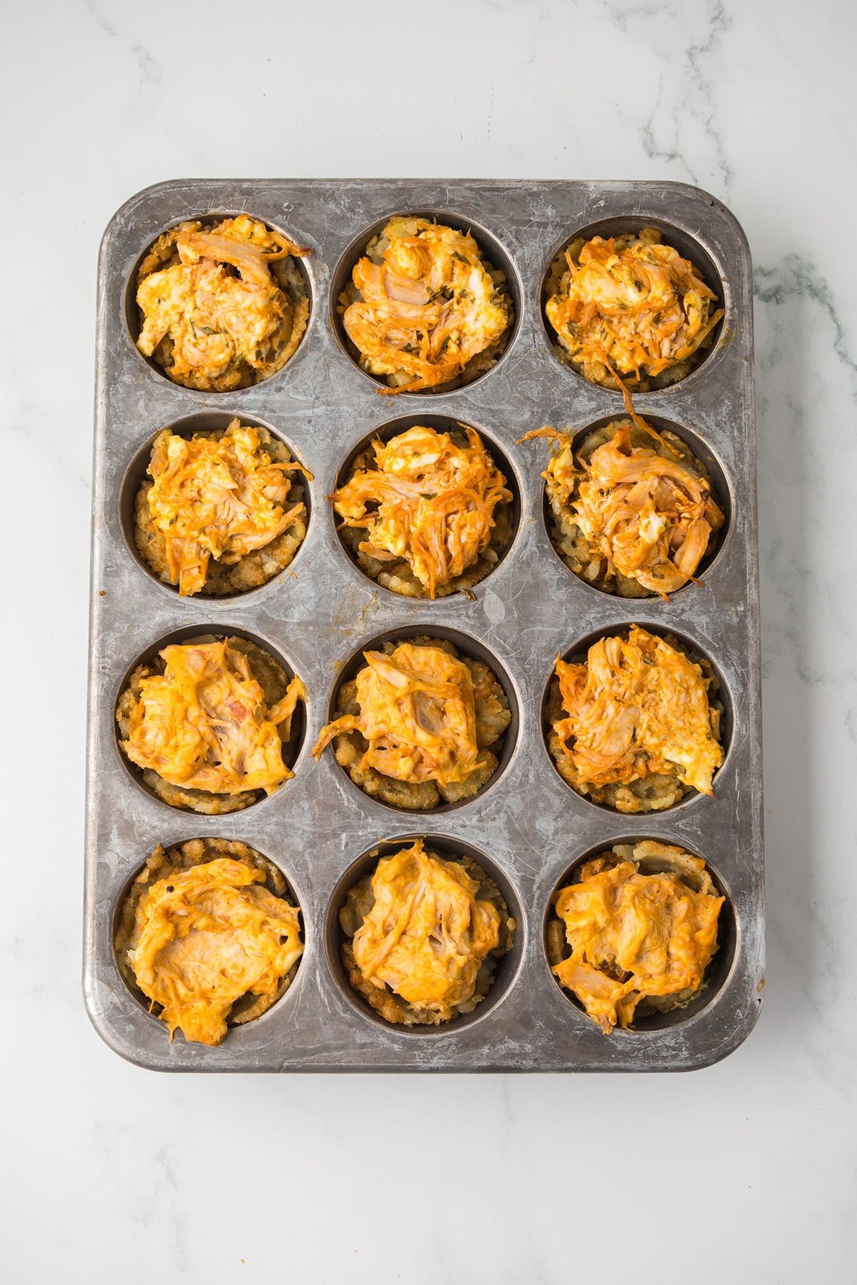 Twelve baked buffalo chicken tater tot cups in a muffin pan.