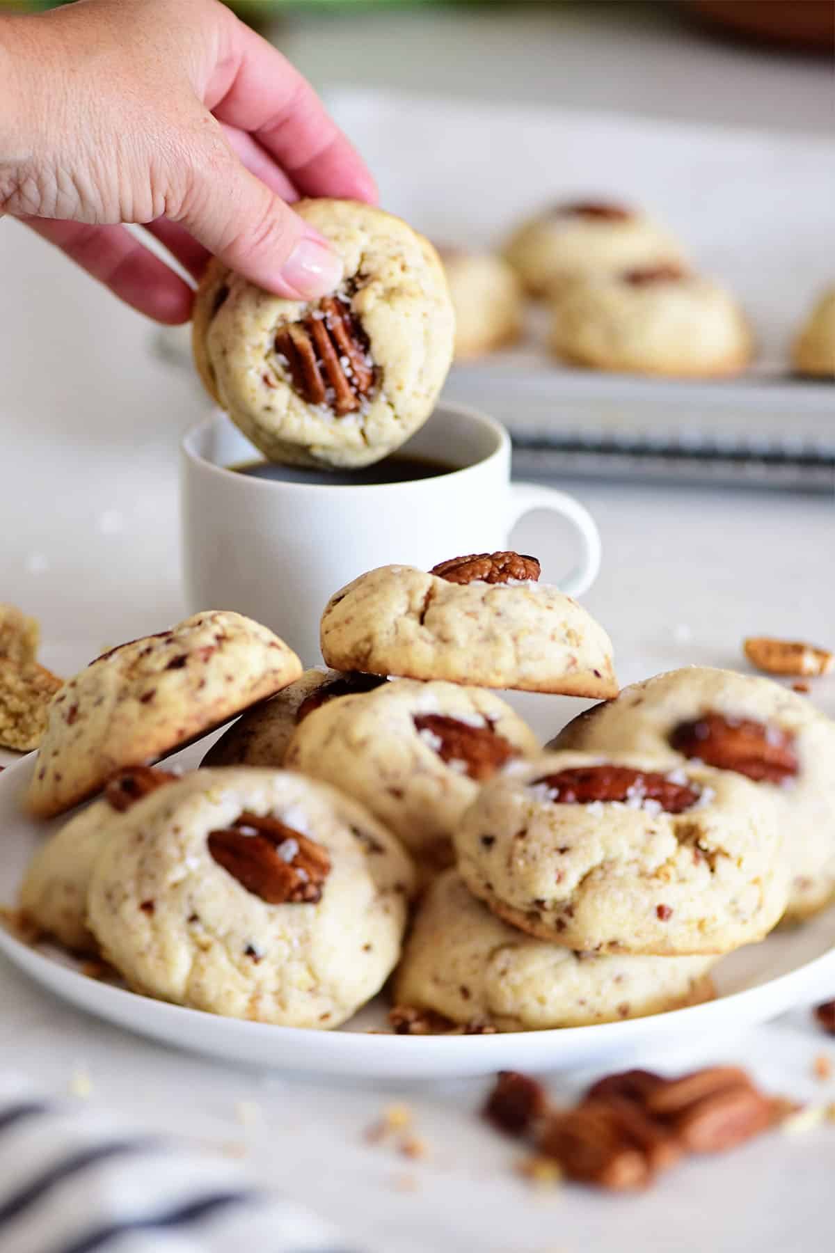 a plate full of homemade Butter Pecan Cookies, one being dunked in coffee