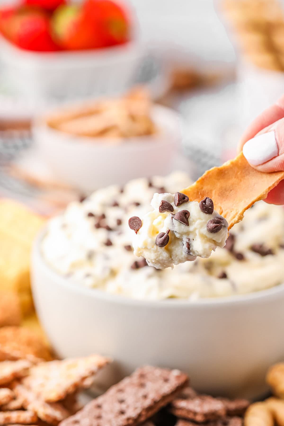 dipping a broken waffle cone into cannoli dip in a white bowl with chocolate chips on top