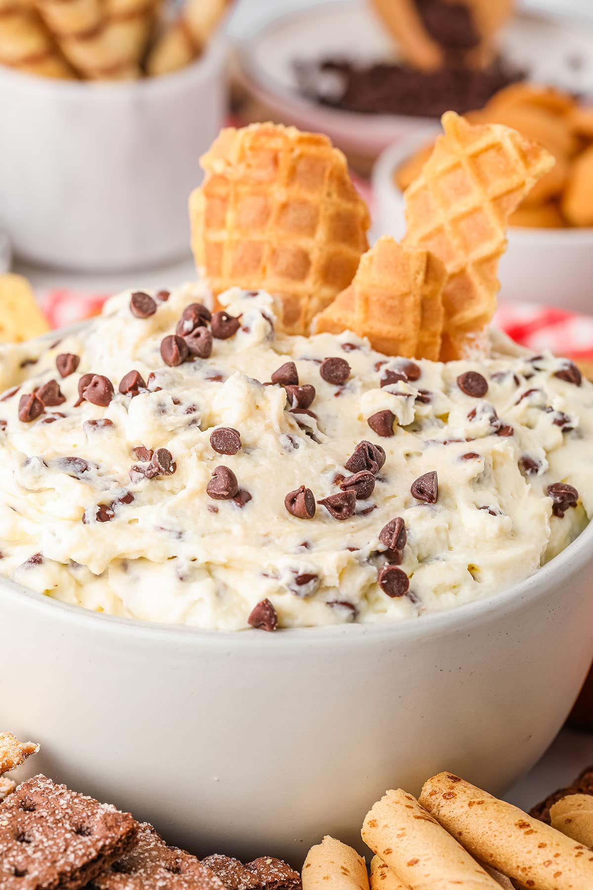 close up of cannoli dip in white bowl with chocolate chips and broken waffle cones on top