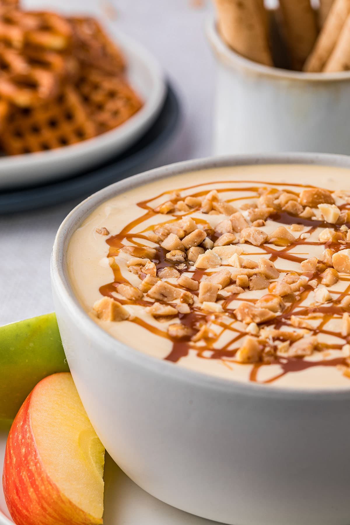 apple dip in a bowl with caramel and chopped peanuts on top