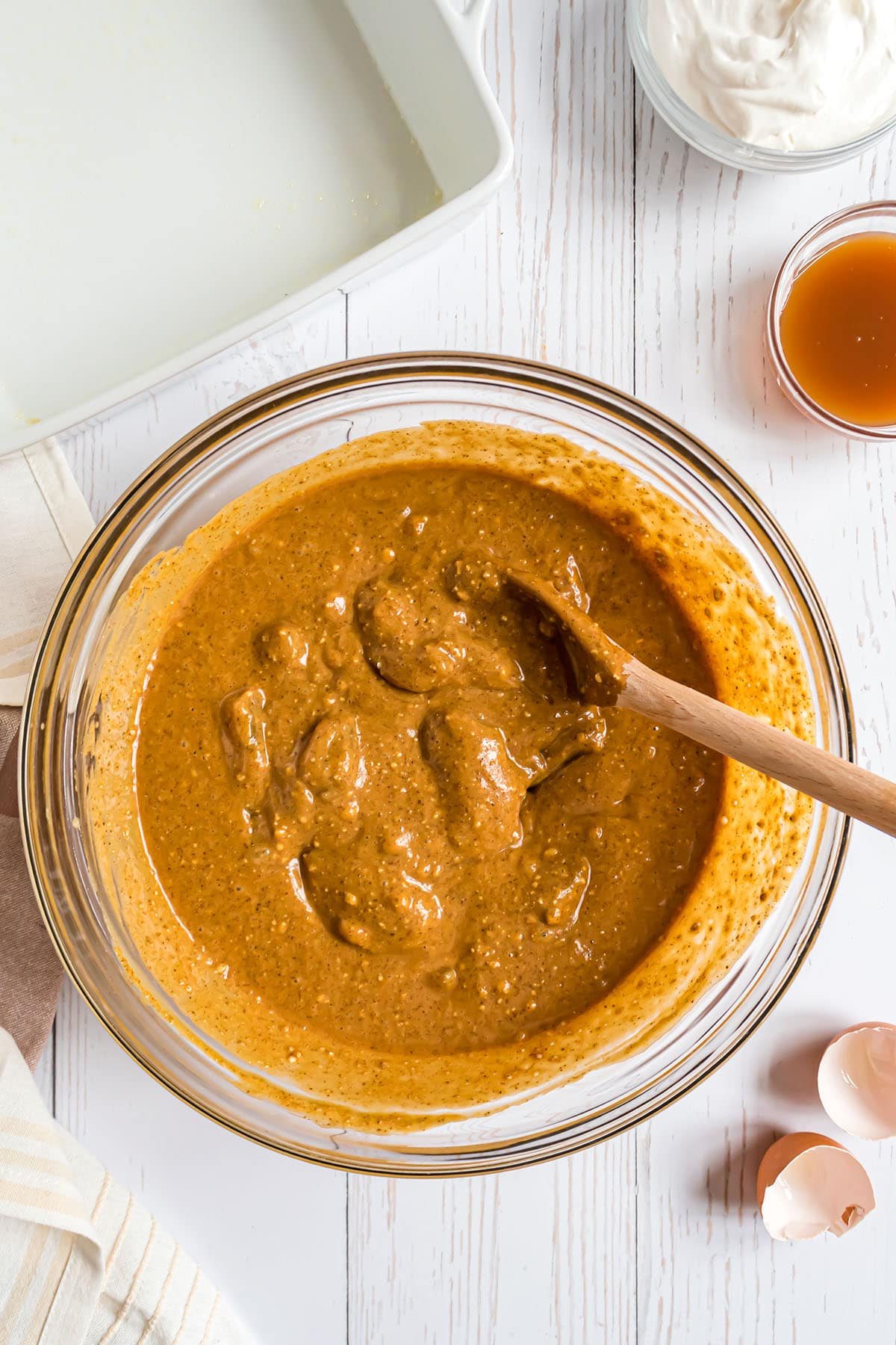 cake batter with apple pie filling in a glass mixing bowl and a wooden spoon