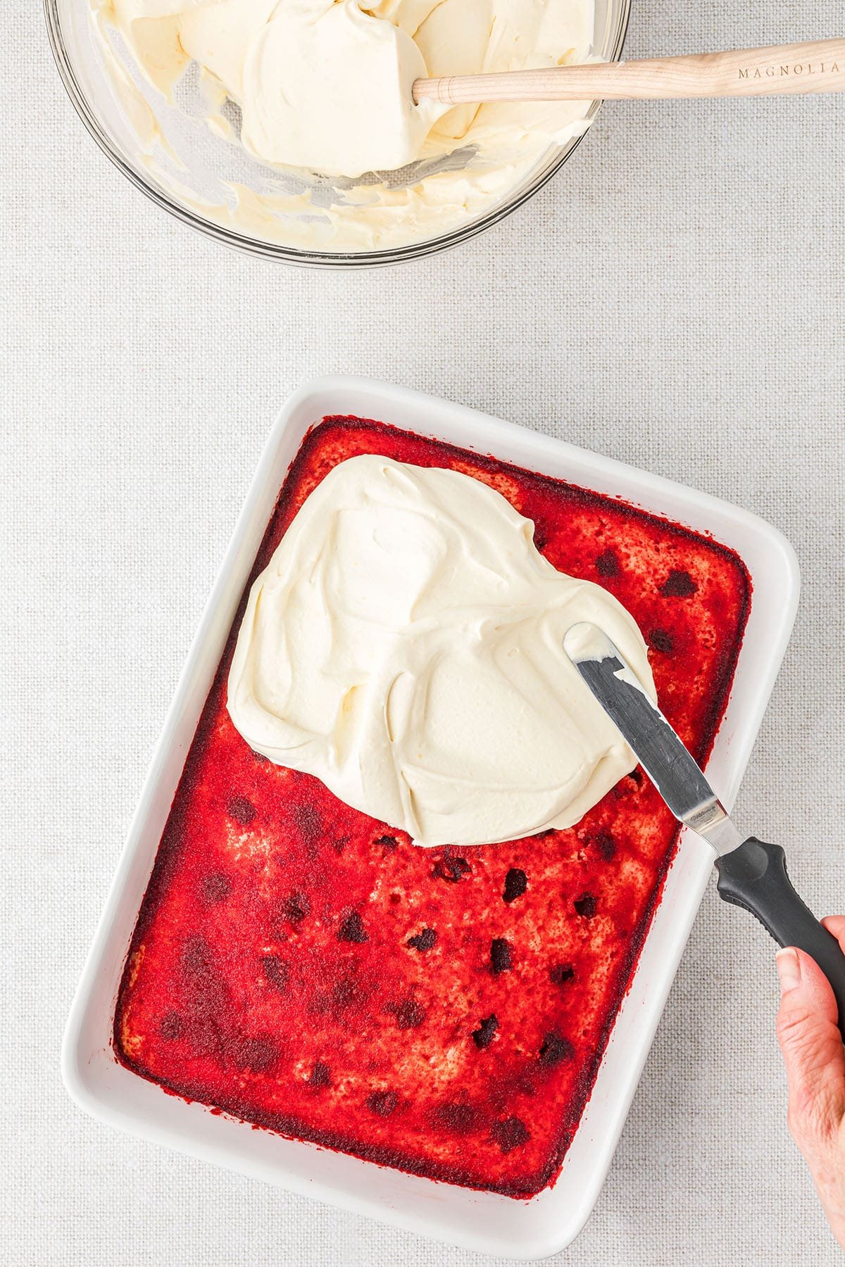 spreading frosting over a cherry jello poke cake