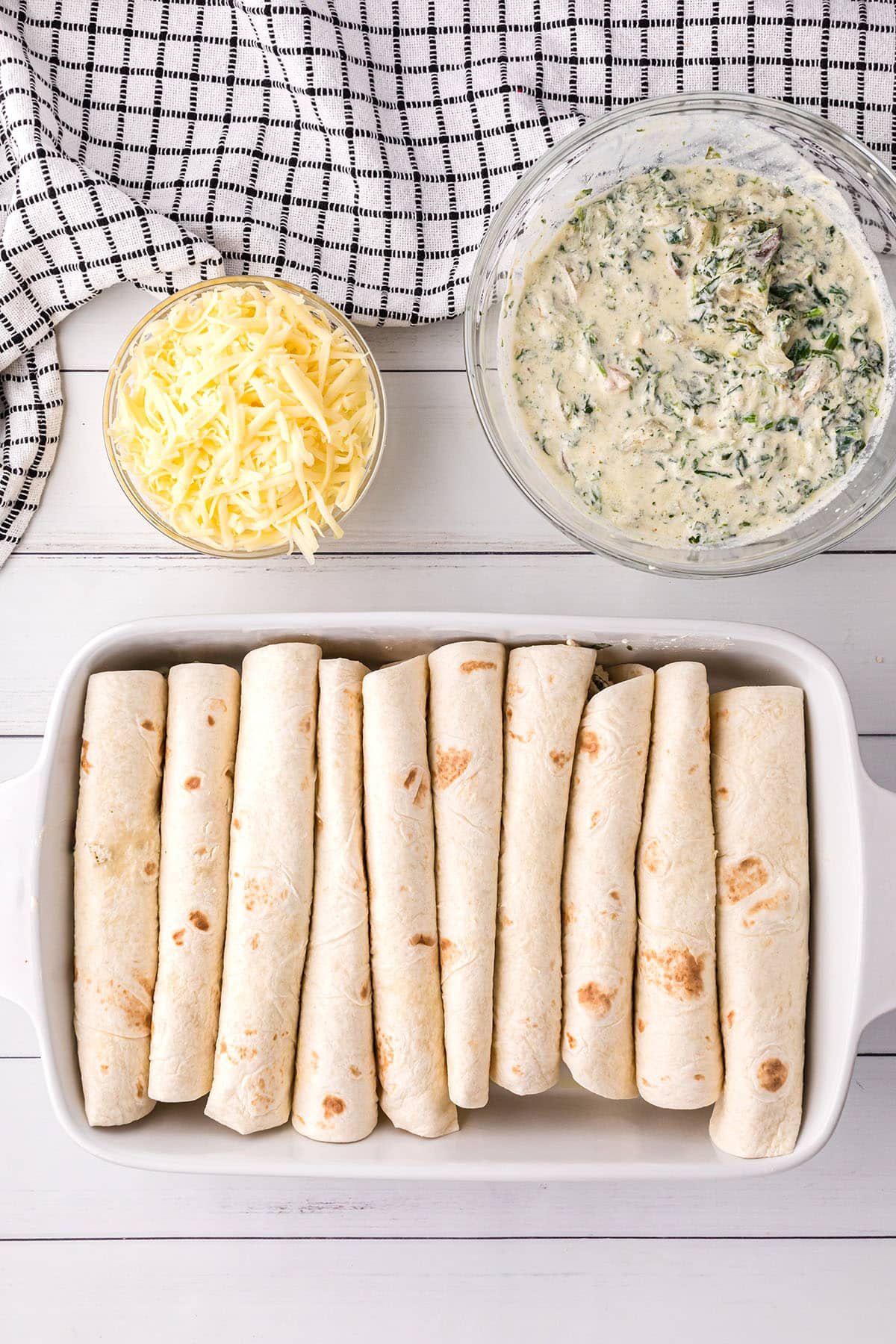 chicken and spinach enchiladas rolled and in a casserole dish