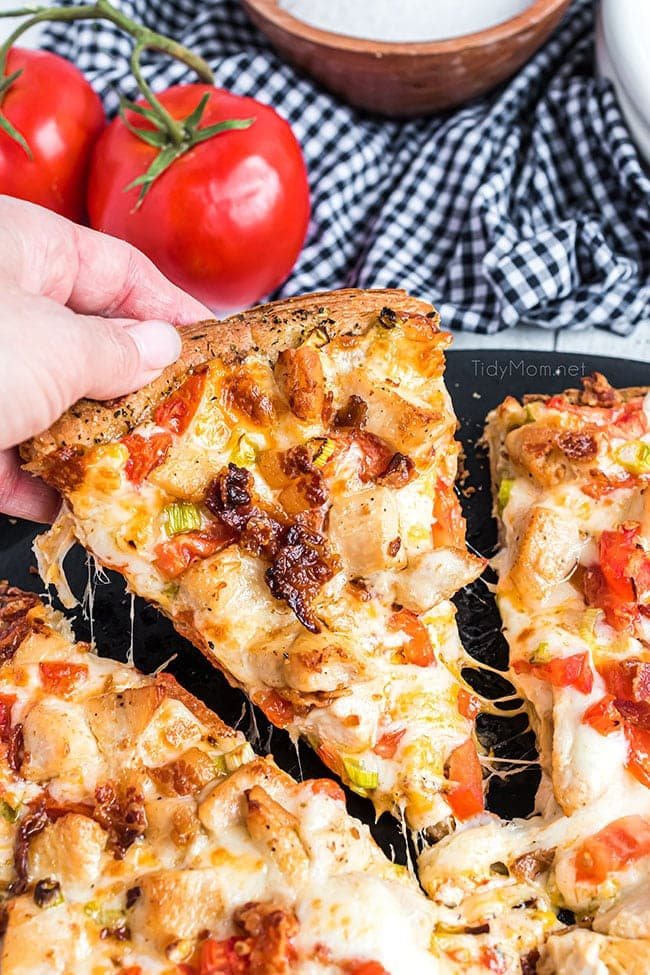 woman's hand holding a sliced of chicken bacon ranch pizza
