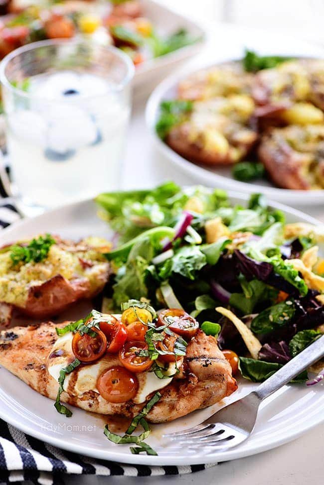 grilled chicken breasts topped with caprese salad on a dinner plate