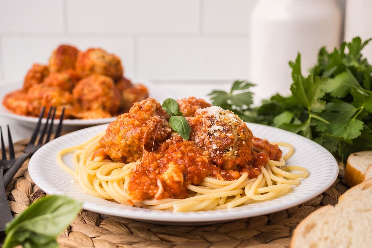 Close-up of chicken Parmesan meatballs over pasta with marinara and fresh basil.