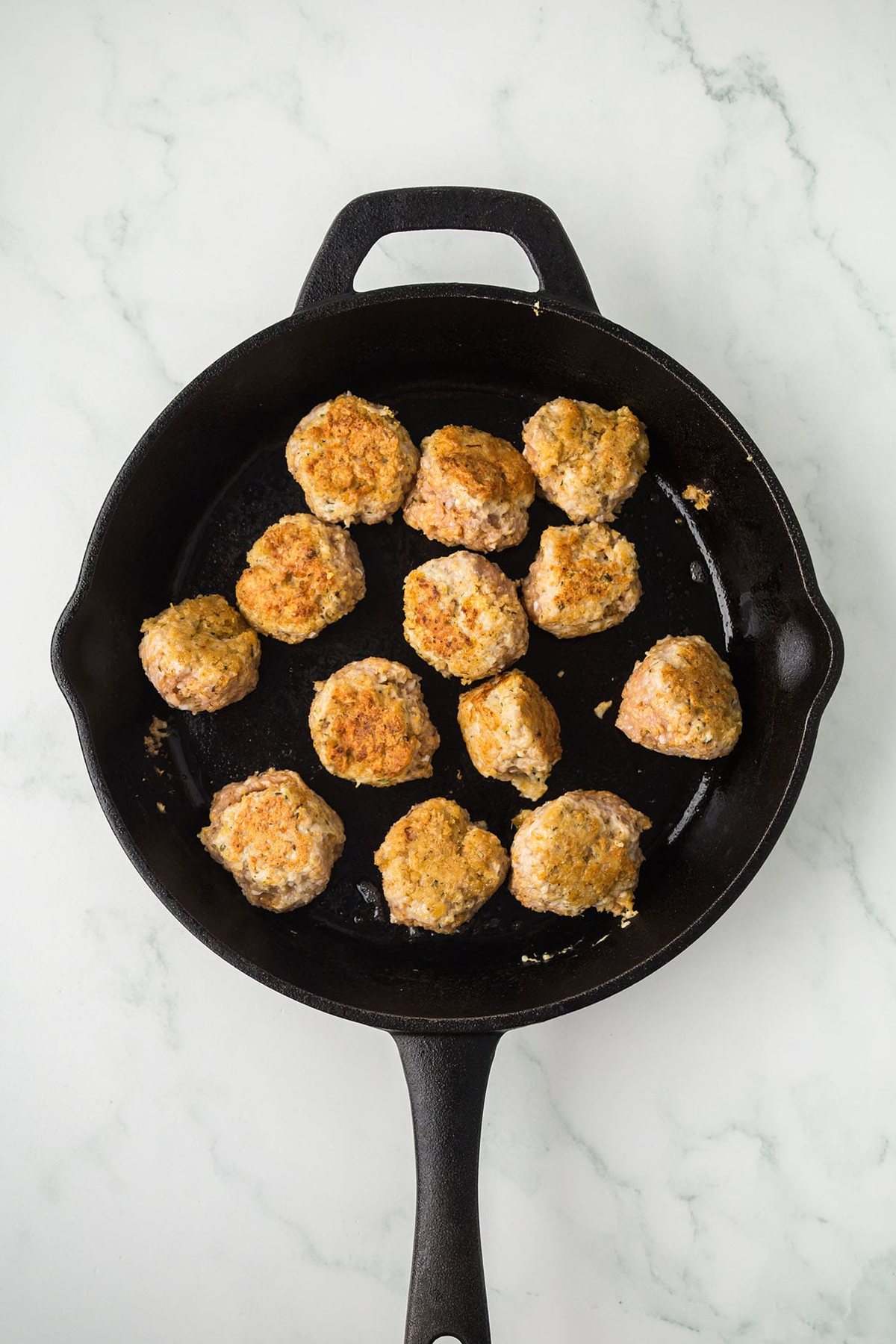 Chicken meatballs browning in a cast iron skillet before adding sauce.