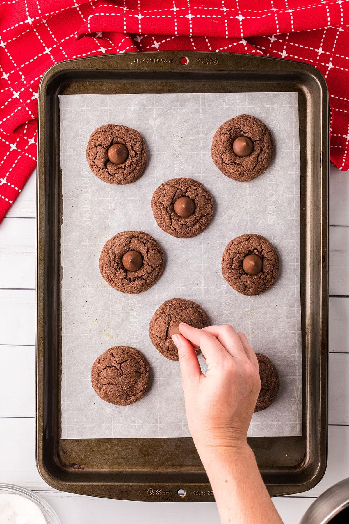 a woman's hand placing chocolate kisses on fresh baked cookies