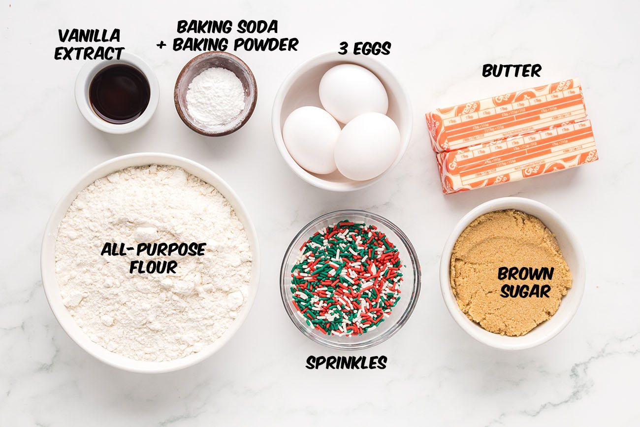 Ingredients laid out on a counter to make Christmas Blondies, including butter, brown sugar, eggs, flour, and holiday sprinkles.