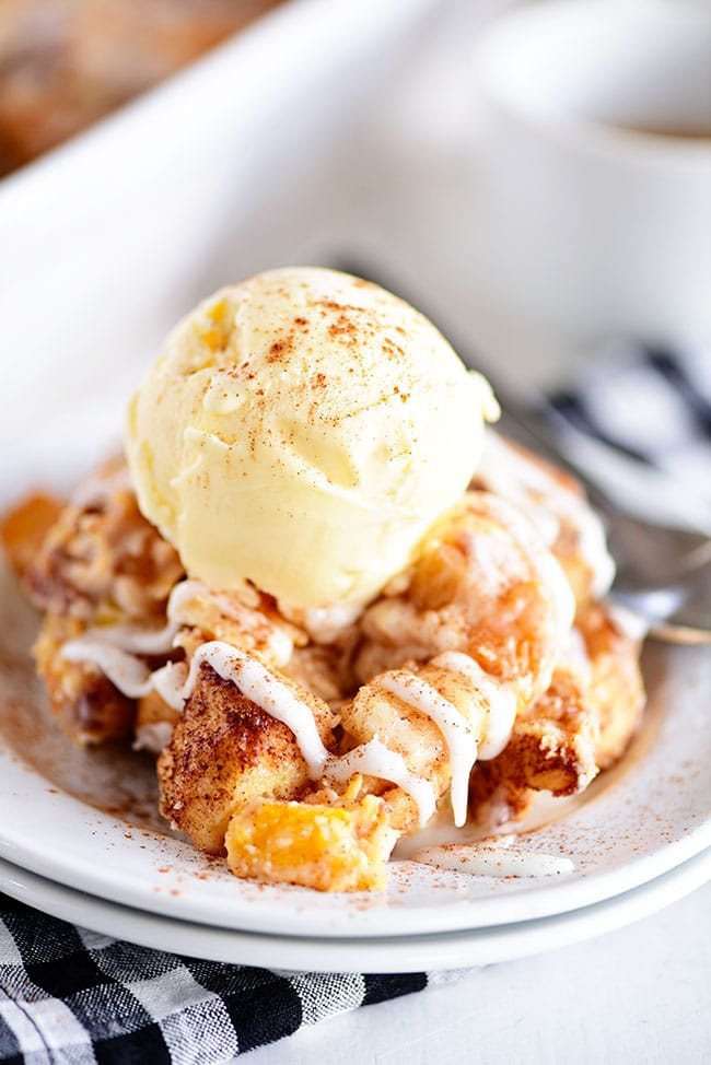 Cinnamon Roll Peach Cobbler topped with ice cream on a white plate