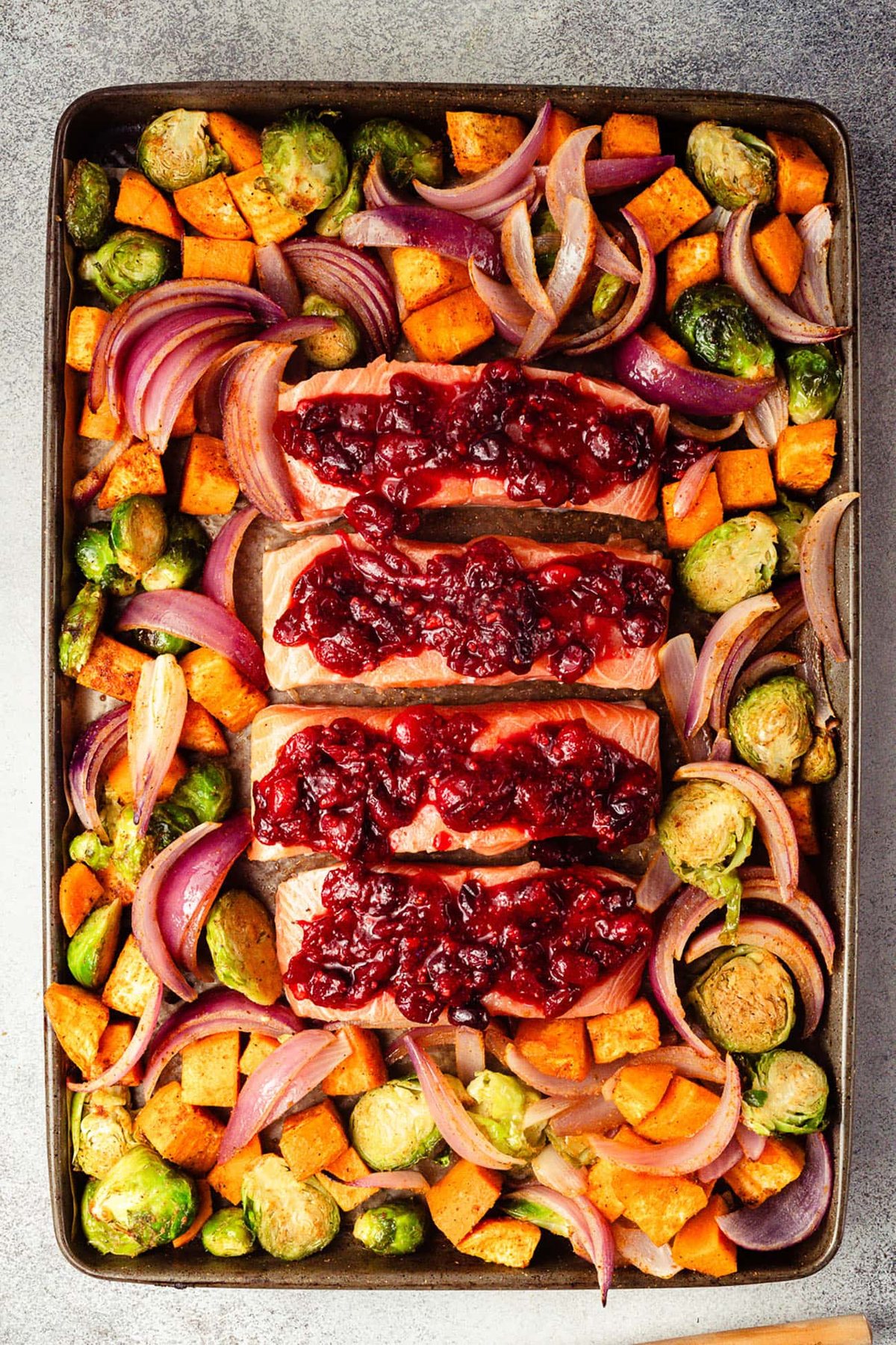 Cranberry orange glaze spooned over salmon fillets on a sheet pan.