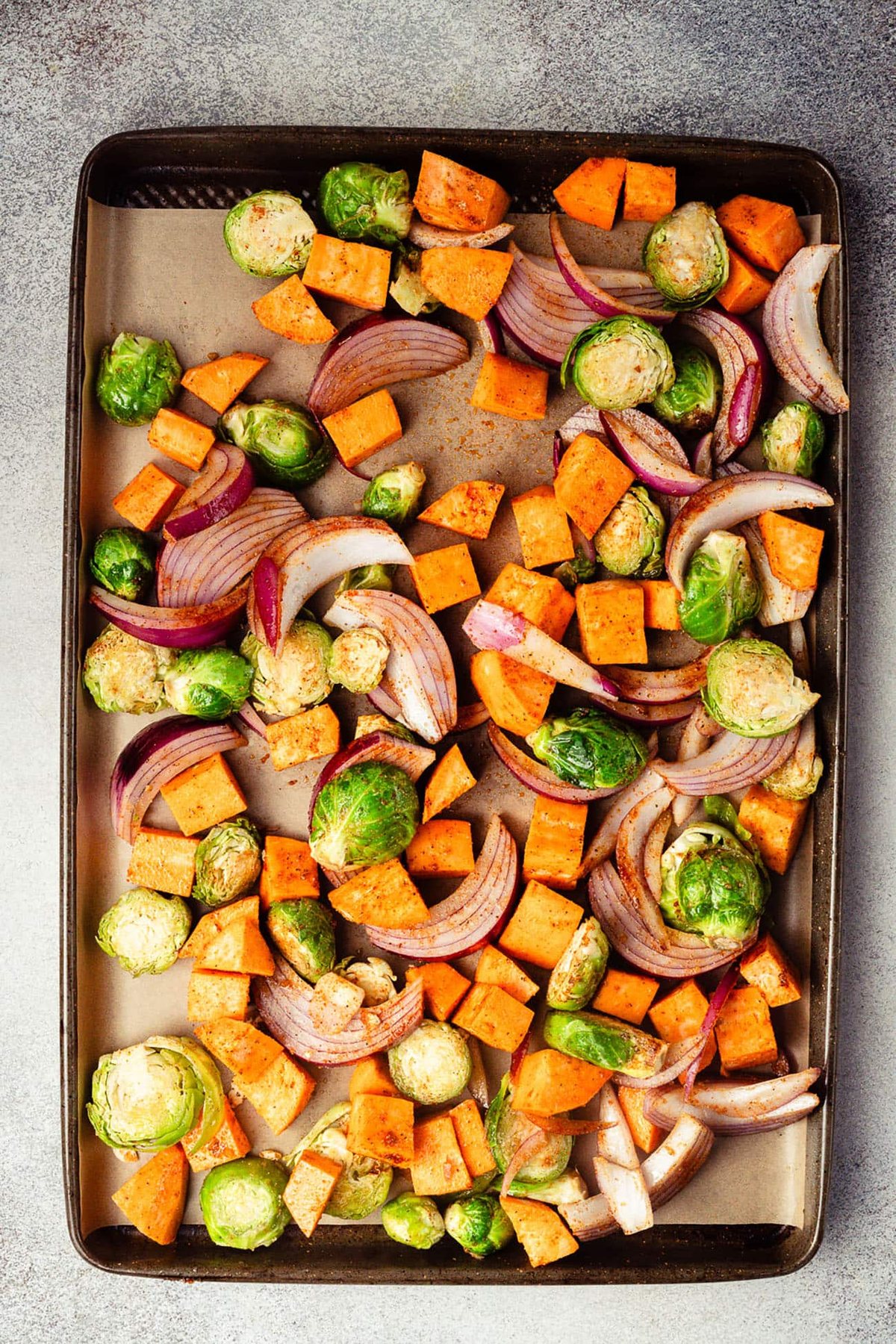 Seasoned sweet potatoes, Brussels sprouts, and red onion on a sheet pan.