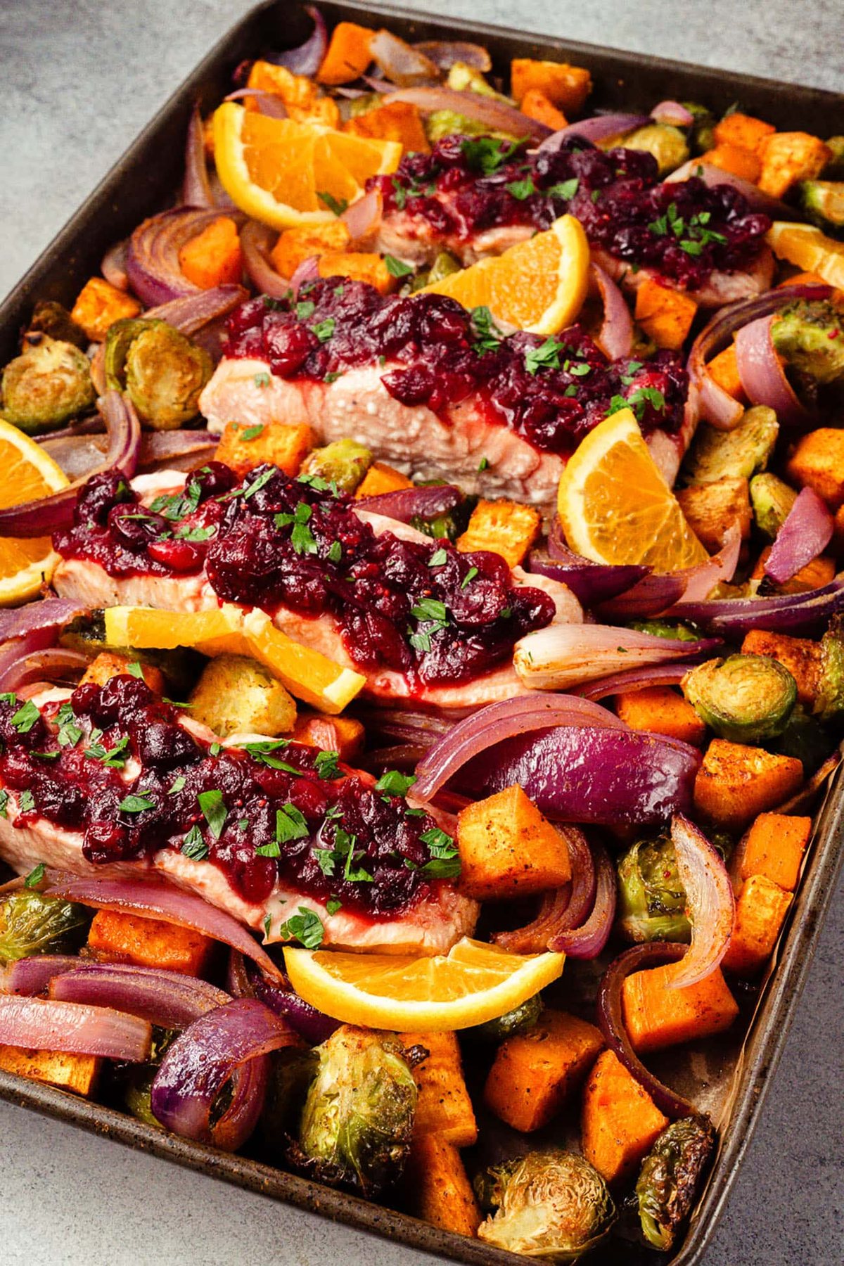 Sheet-pan cranberry orange salmon with roasted vegetables and orange slices.