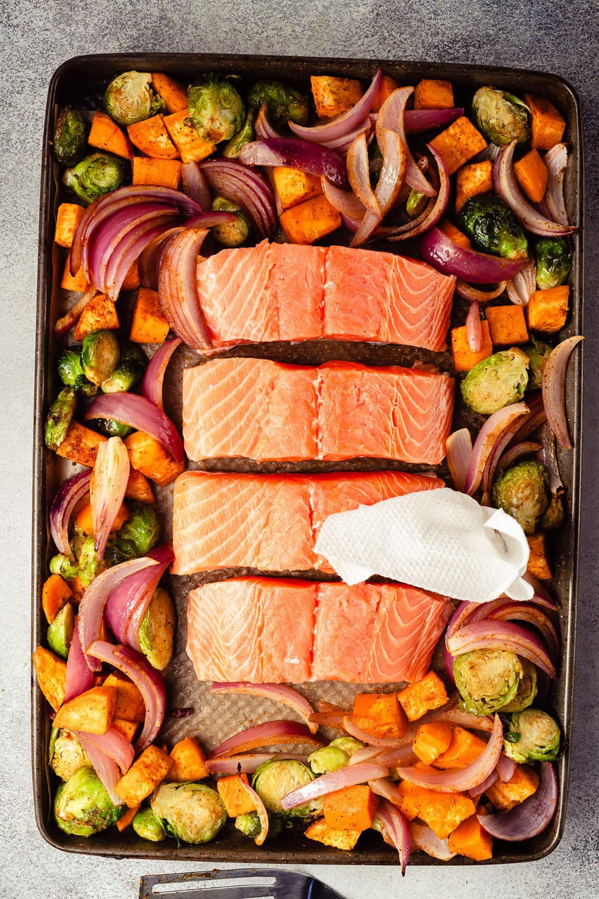 Raw salmon fillets arranged with seasoned vegetables on a sheet pan.