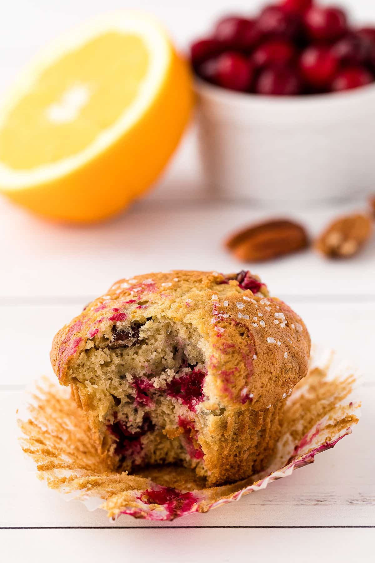 wrapper pulled back on a muffin with a bite out and fresh cranberries and orange in background