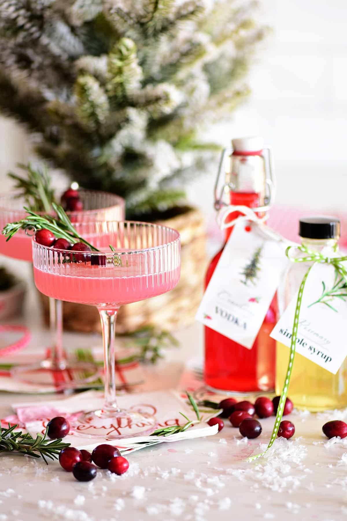 cranberry cosmo cocktail in a coupe glass next to a bottle of homemade cranberry vodka