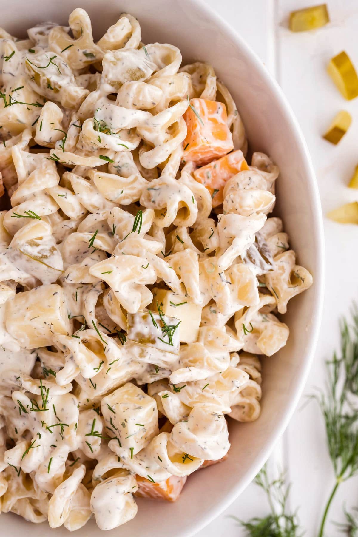 Pasta salad in a white serving bowl with fresh dill next to the bowl.