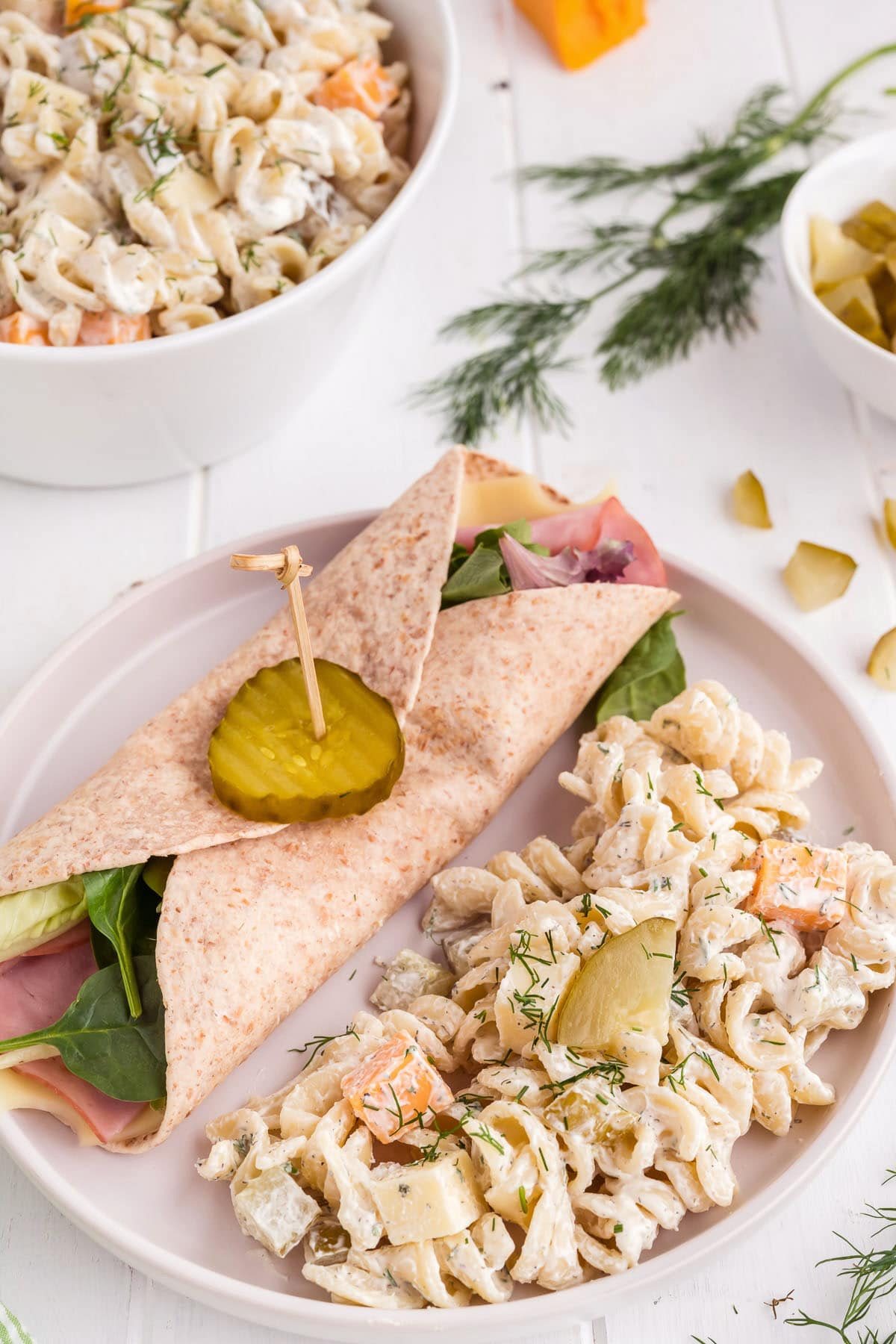 Pickle pasta salad on a white plate alongside a sandwich wrap