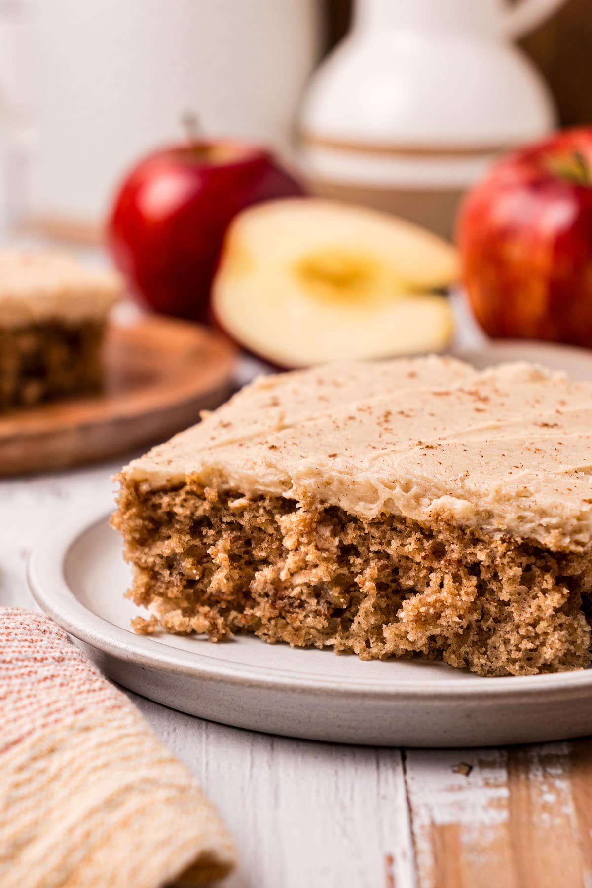 slice of cake on a plate. Red apples in the background.