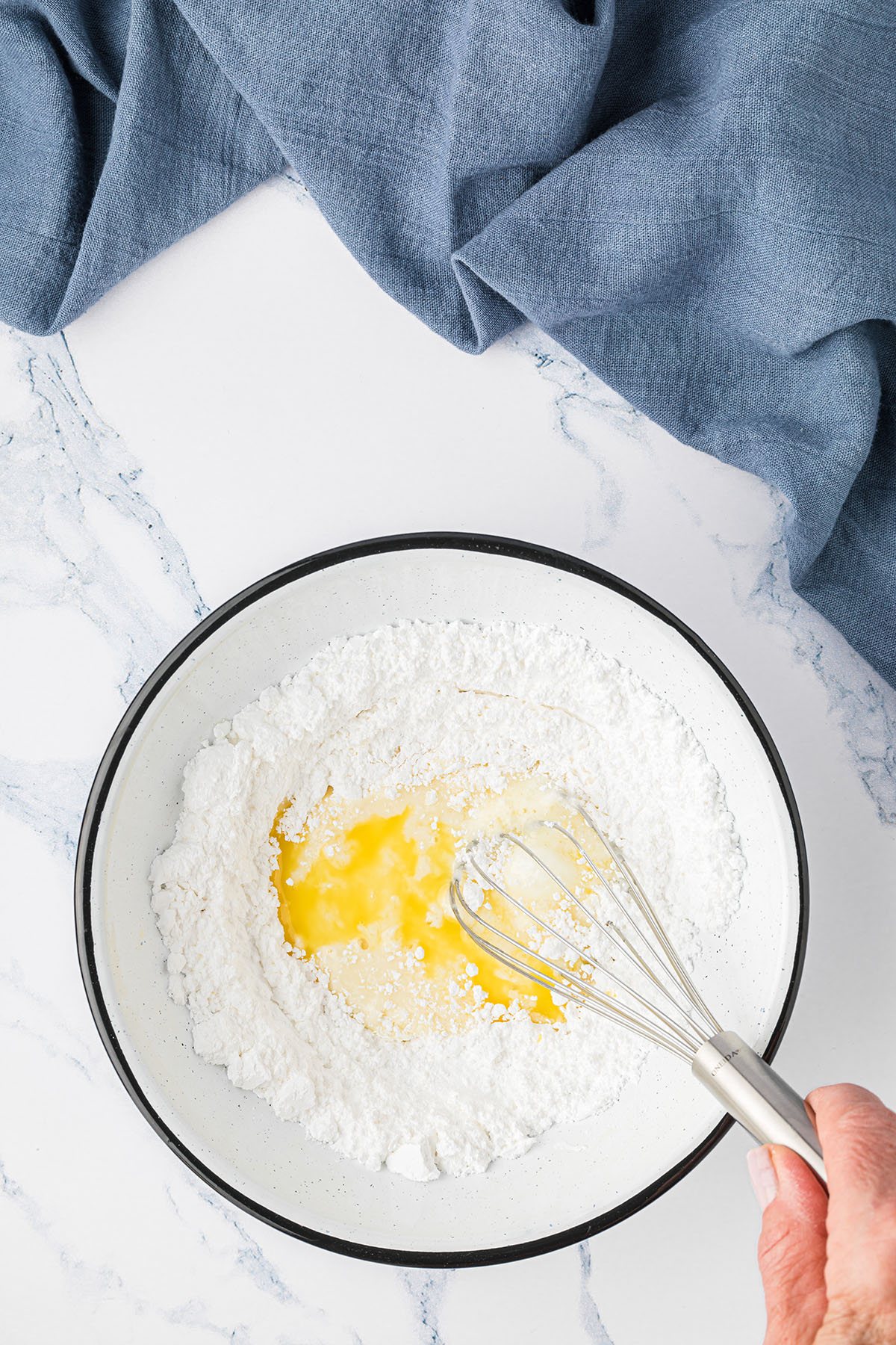 mixing icing for muffins in a bowl with a wire whisk and a blue towel in background