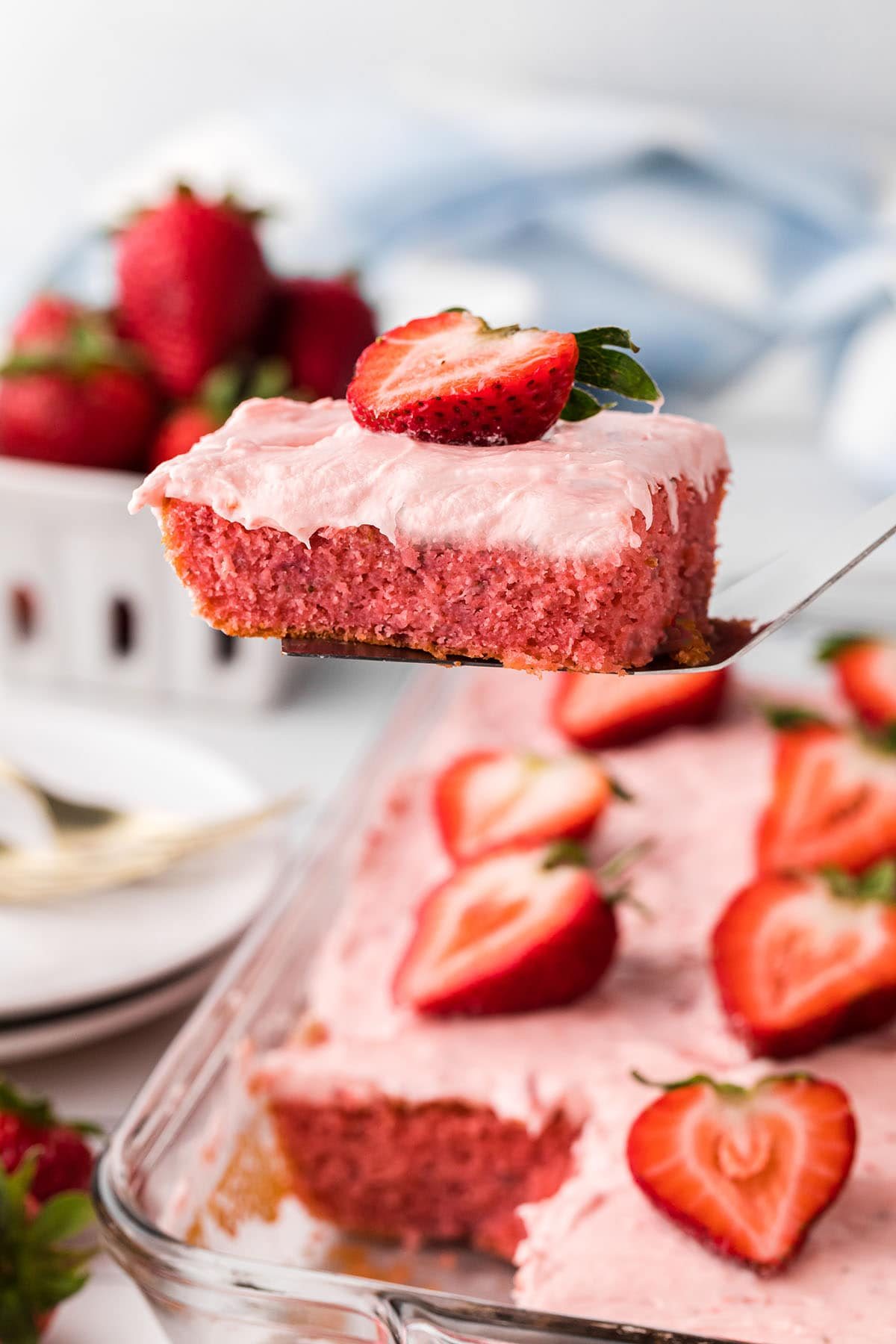 a piece of strawberry cake with butter cream on a spatula over the cake dish.