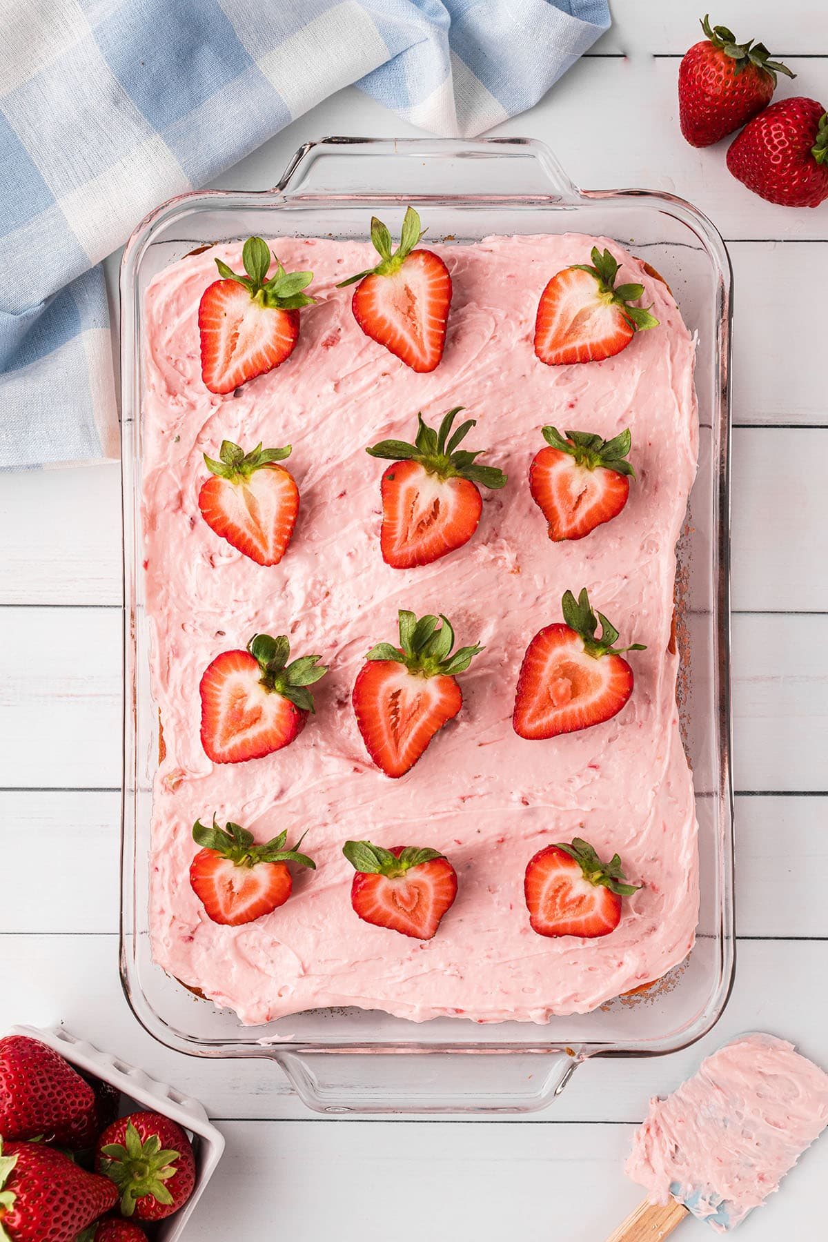 sheet cake in a glass pan topped with strawberry butter cream frosting and fresh strawberries to garnish