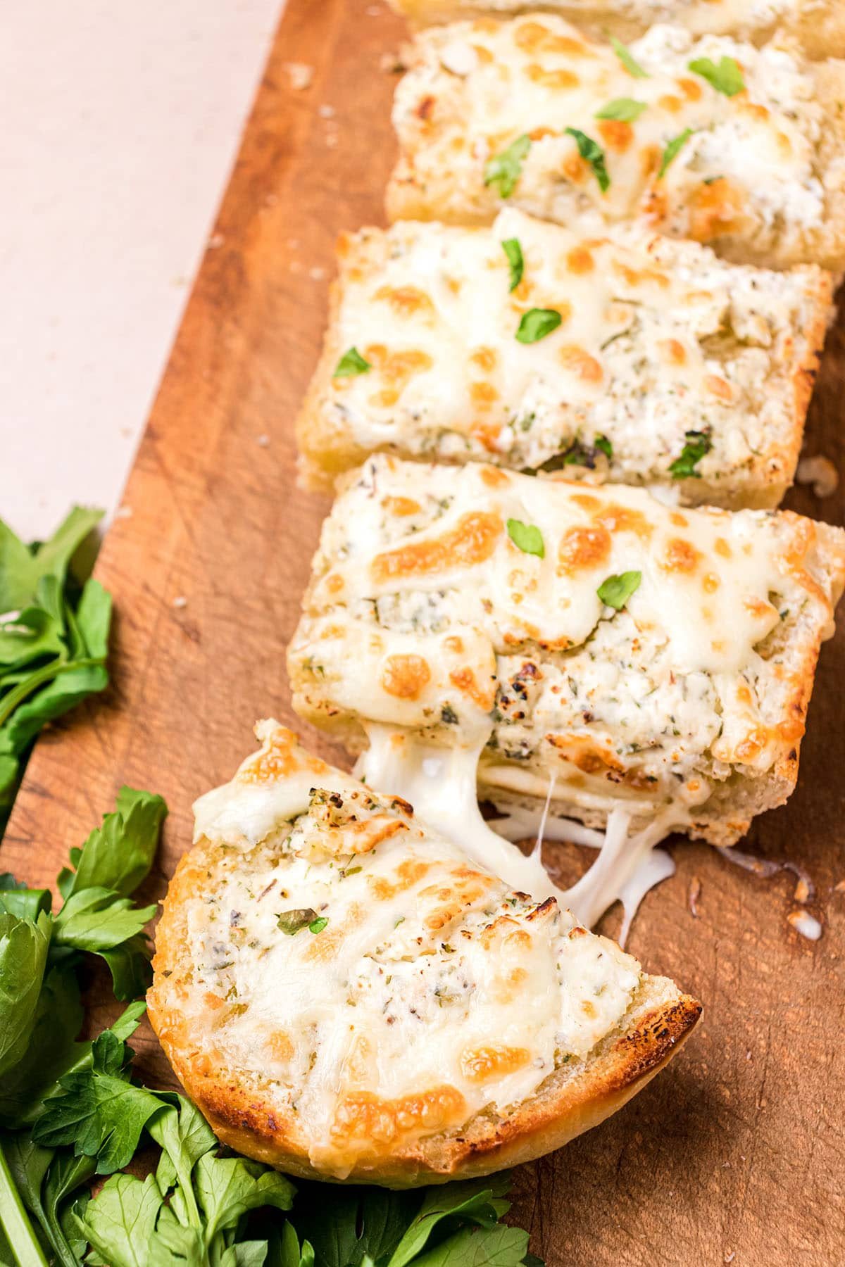Cheesy garlic bread cut and pulled apart on a cutting board