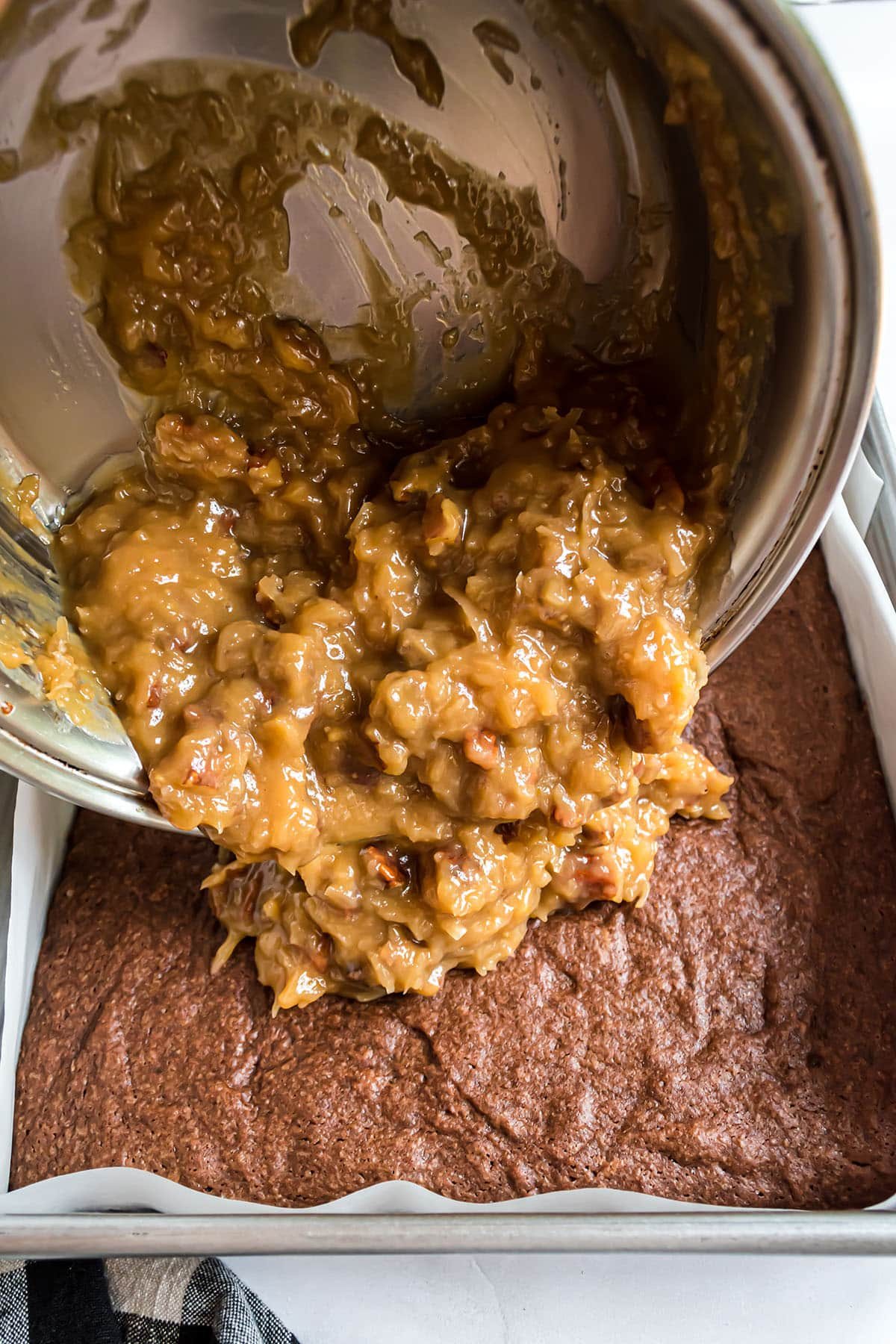 coconut pecan topping being poured over German chocolate brownies.