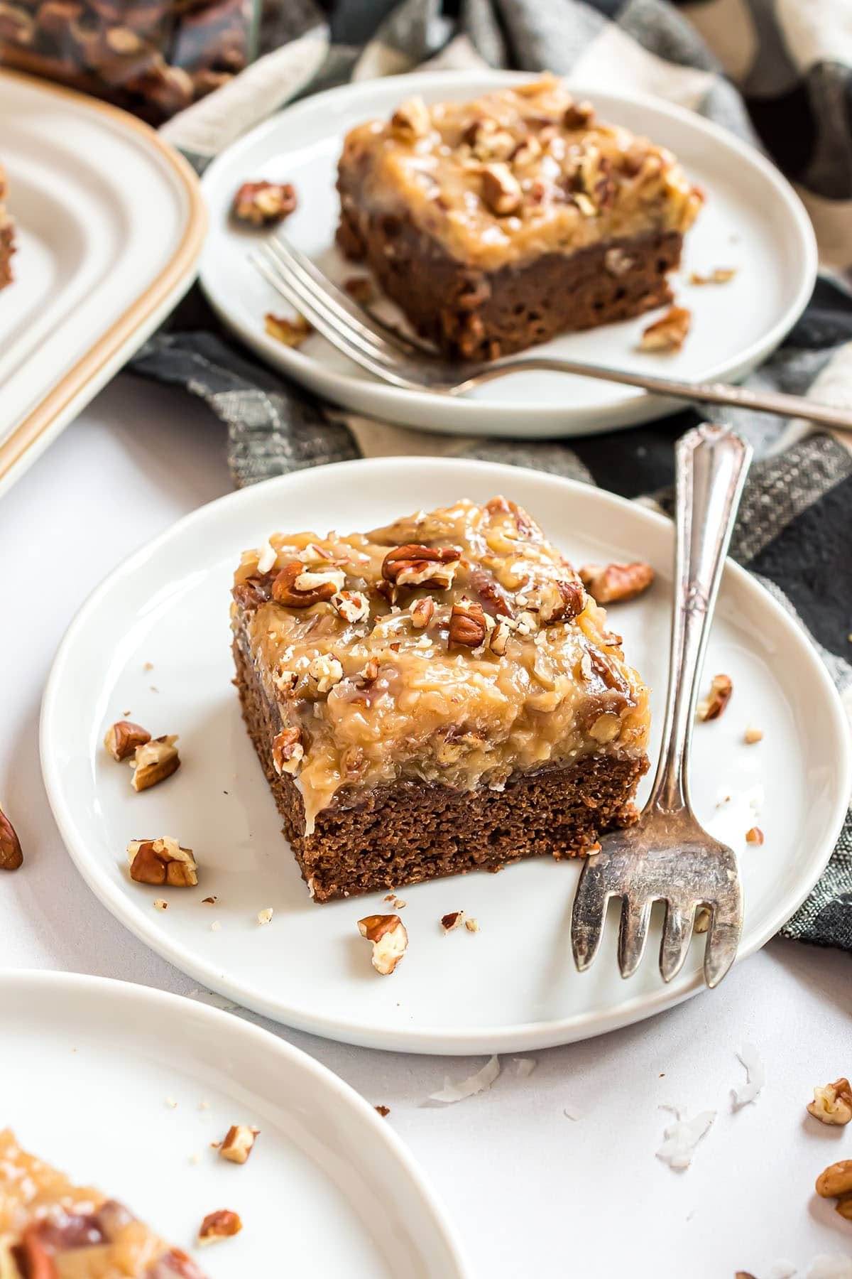 2 servings of brownies with pecan frosting on white plates with forks.