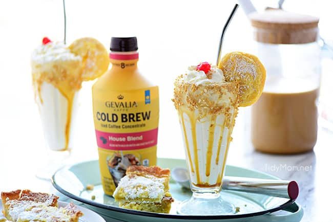 Gooey Butter Cake Cold Brew Milkshake in a glass with straw and bottle of Gevalia Cold Brew Concentrate and gooey butter cake and ice cream scooper on tray.
