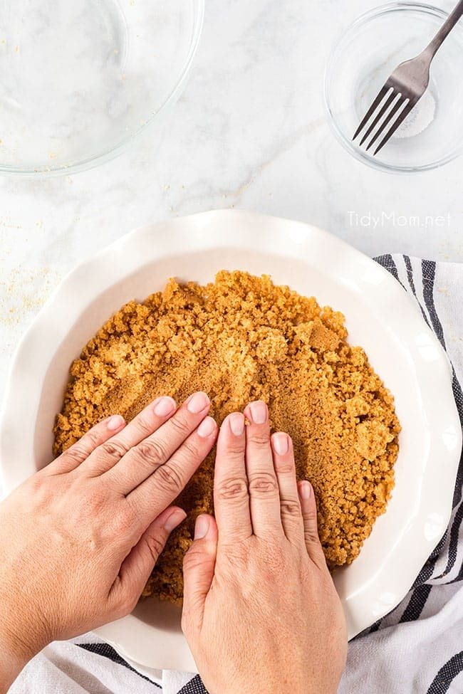 woman pressing graham cracker crust in a white pie dish