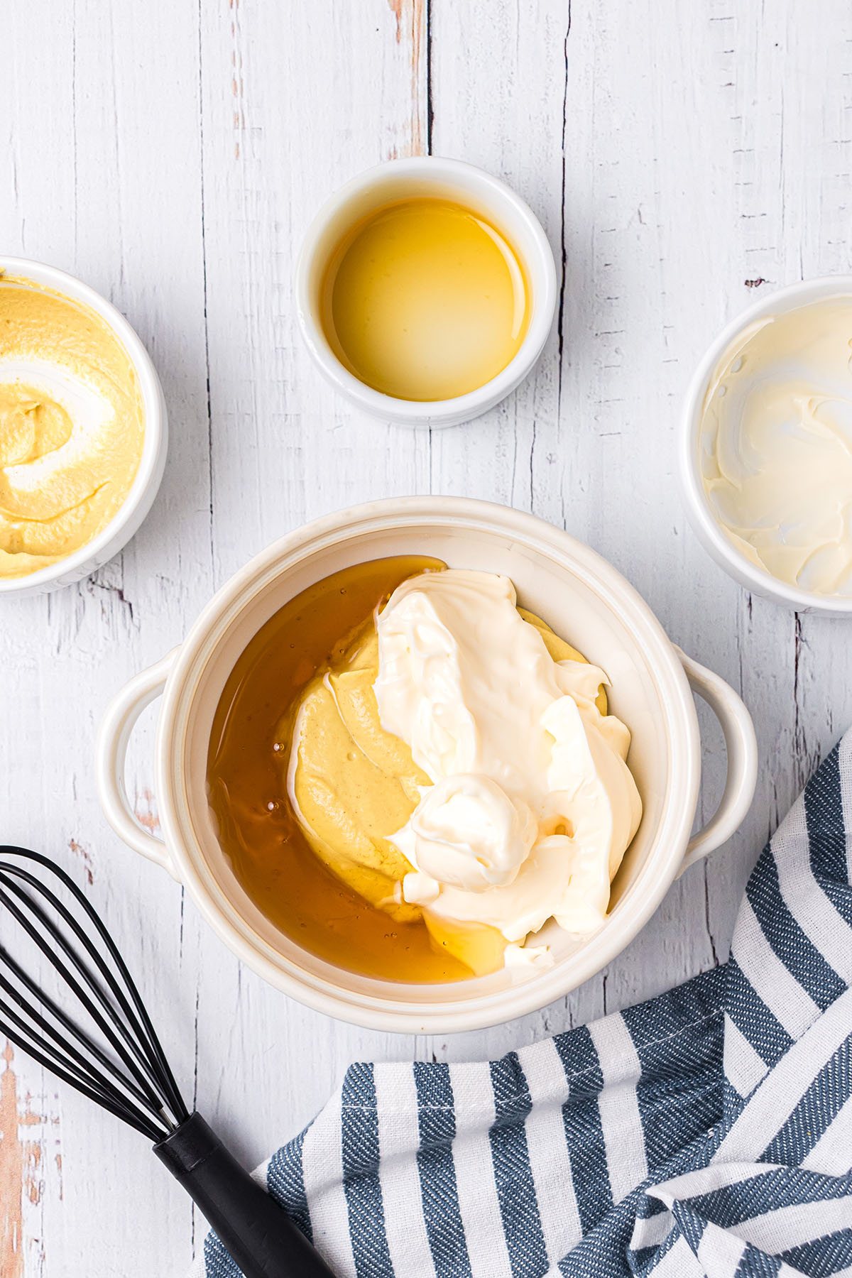 making honey mustard sauce in a small white bowl with a wire wisk and a blue and white towel