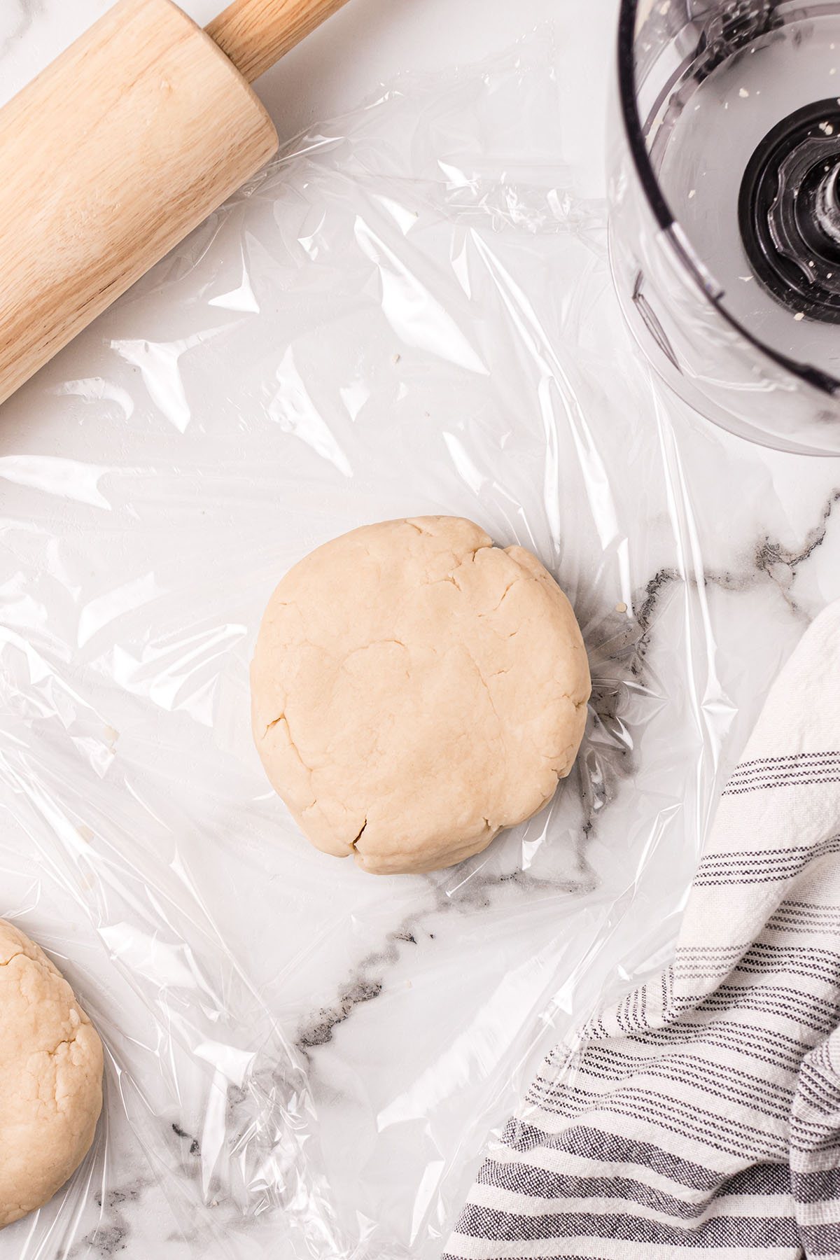 pie dough disk on counter with plastic wrap and a rolling pin next to it