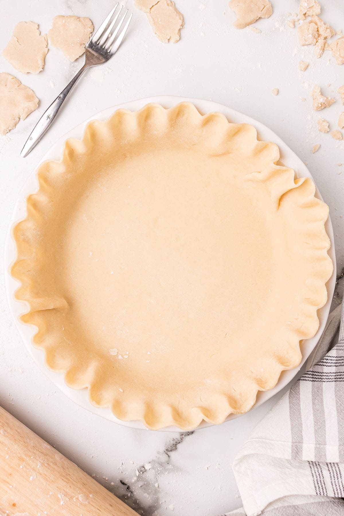 crimped pie crust on a white counter with a black and white towel next to it