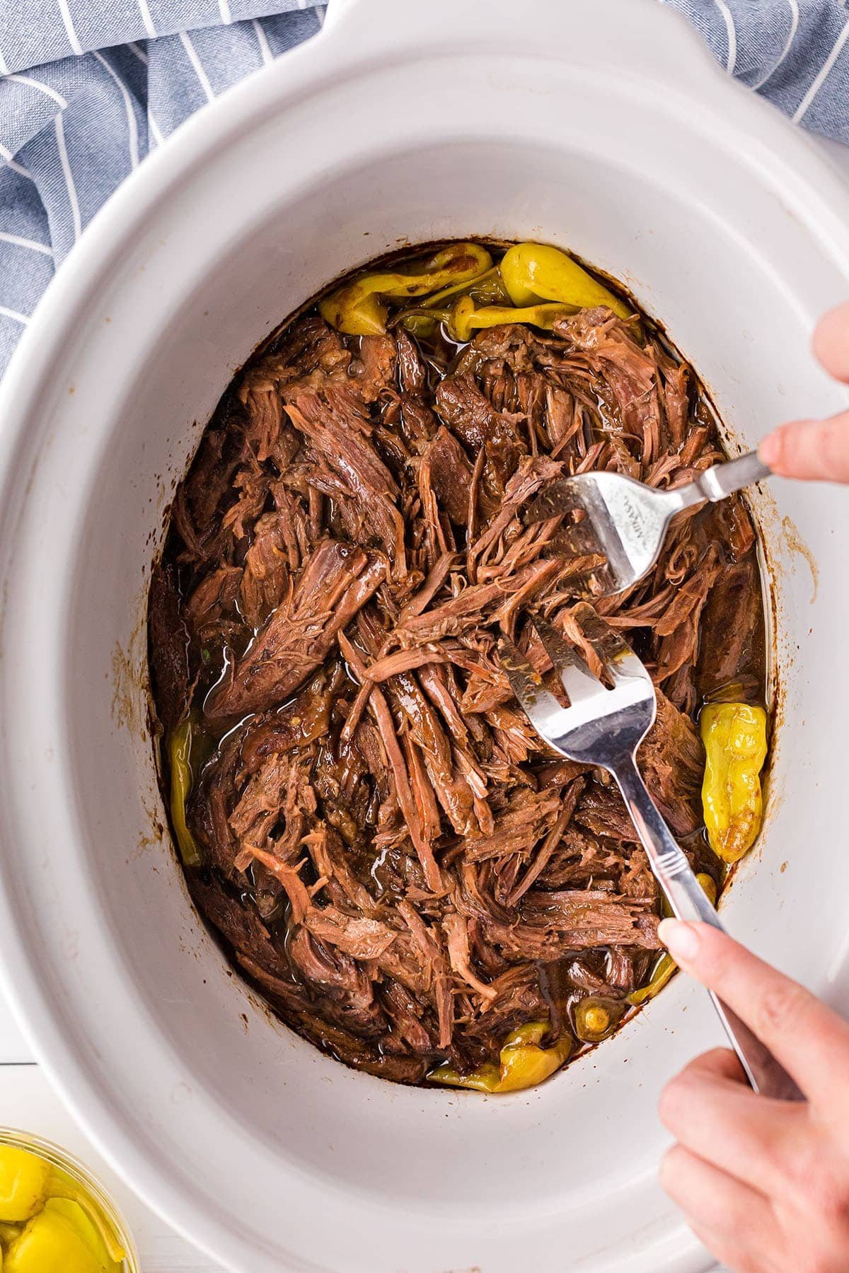 2 forks shredding pot roast in a white slow cooker
