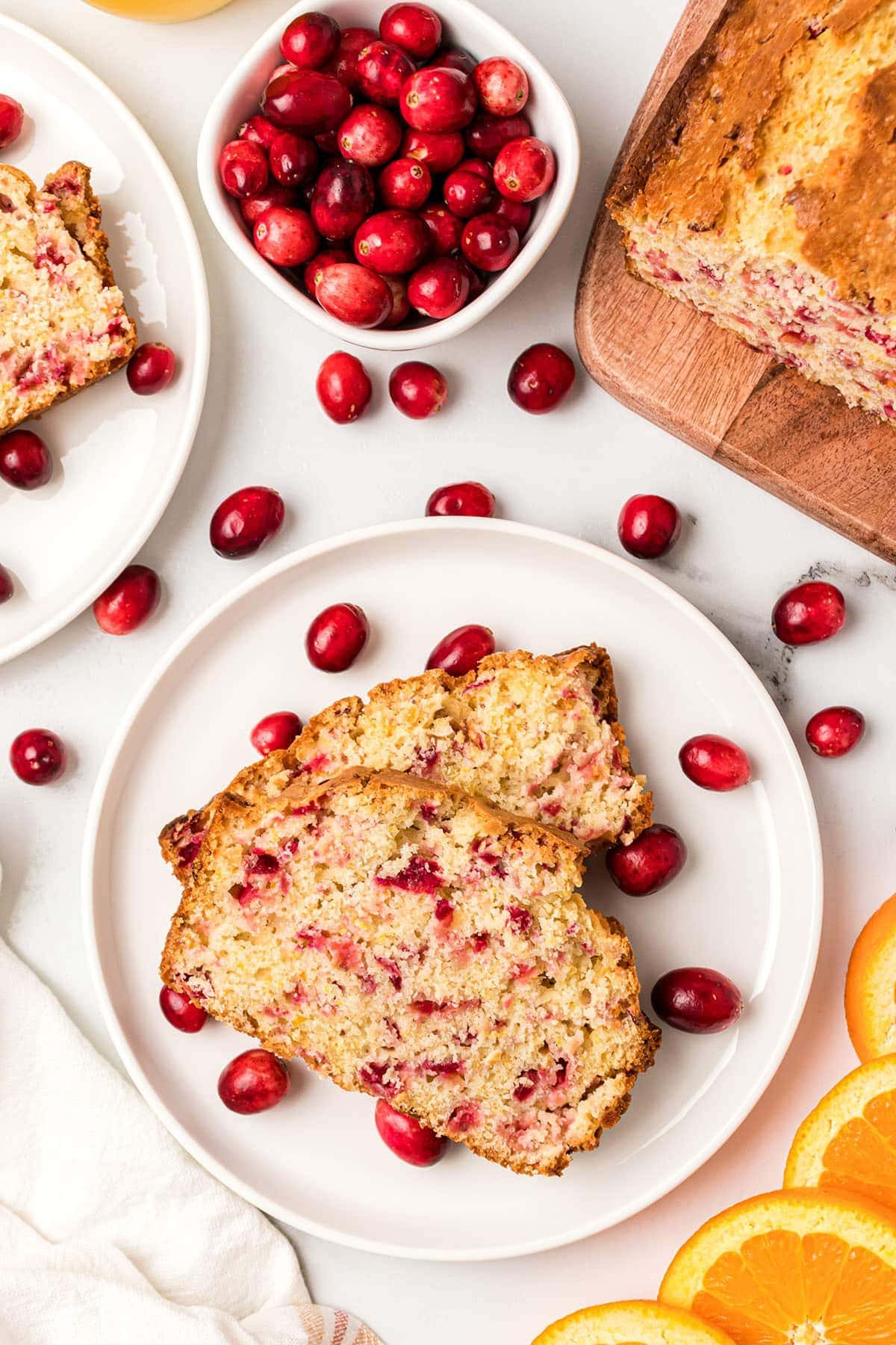 Orange Cranberry Quick Bread on a plate with fresh orange slices and cranberries