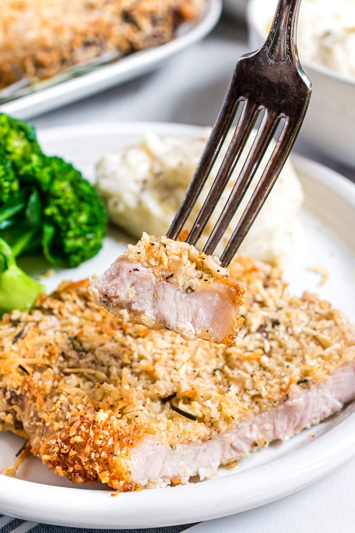 parmesan crusted pork chop on a dinner plate with a bite on a fork