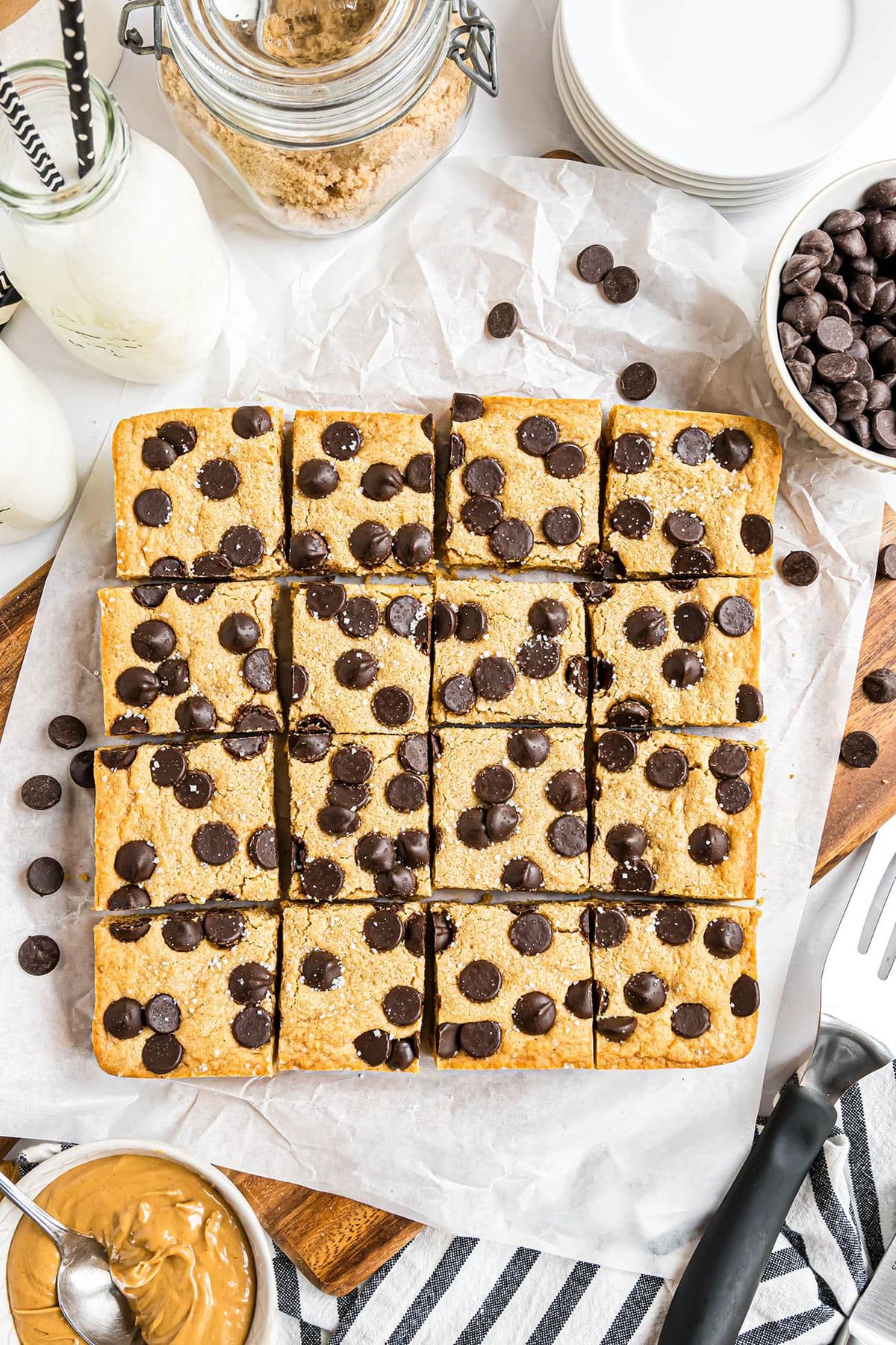 Overhead shot of cut peanut butter blondies arranged in a square on parchment paper, surrounded by milk and baking ingredients.