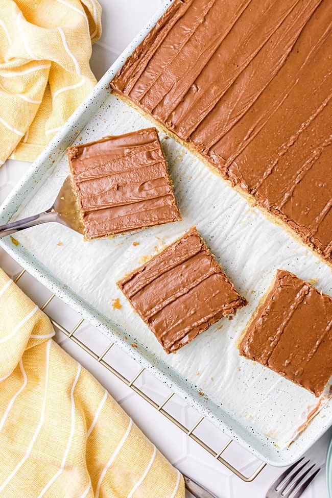 Peanut butter Texas sheet cake with chocolate frosting on a half sheet pan and 3 slices cut