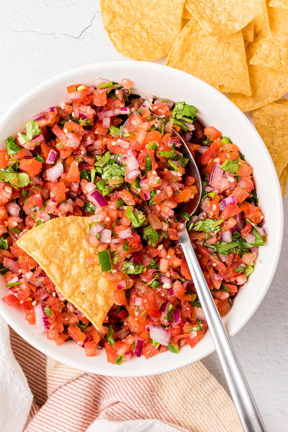 pic de gallo in a white bowl with a tortilla chip and spoon